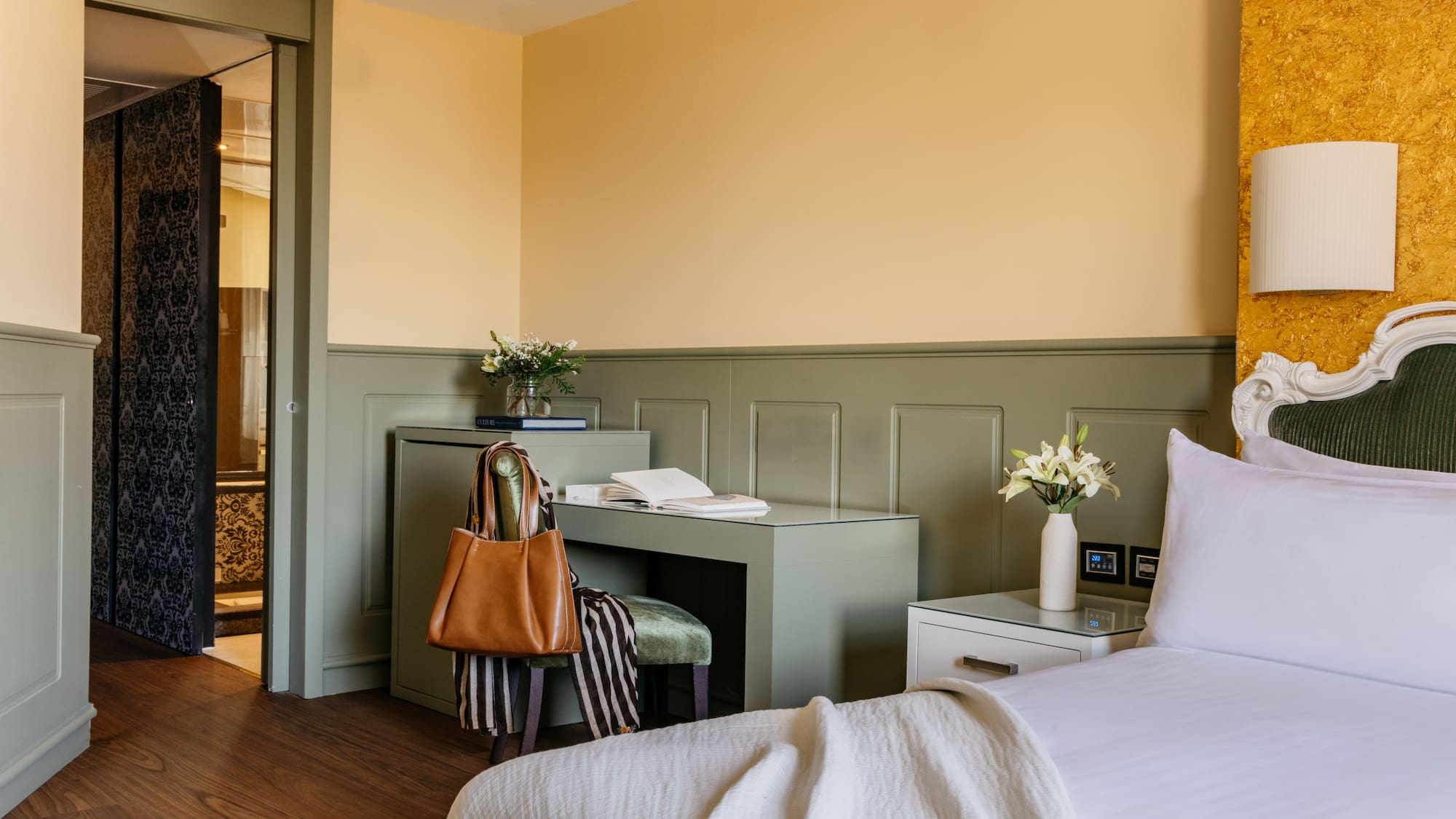 Habitación de hotel elegante con cama, escritorio verde, paredes amarillas y puerta de baño.