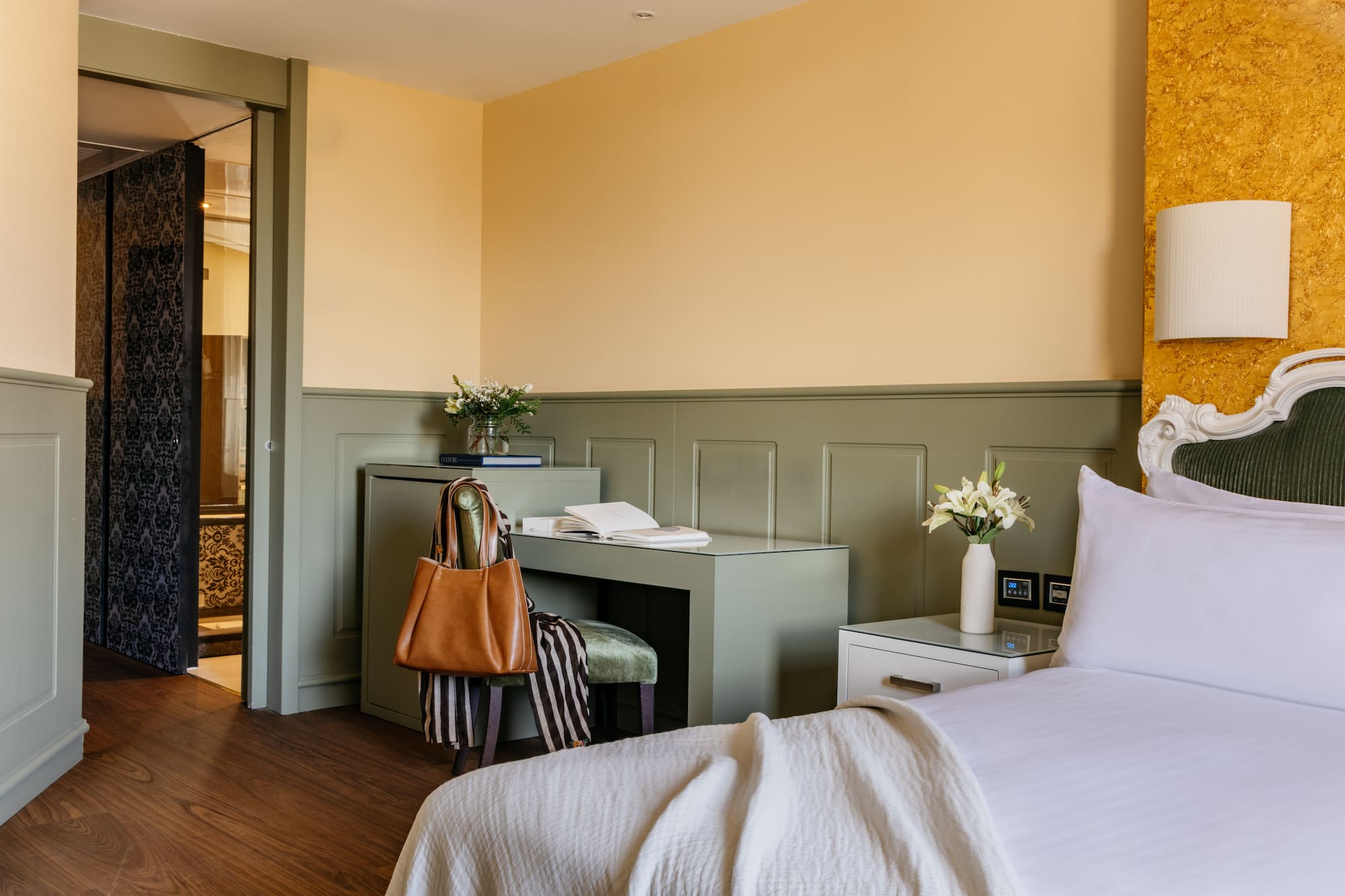 Habitación de hotel elegante con cama, escritorio verde, paredes amarillas y puerta de baño.