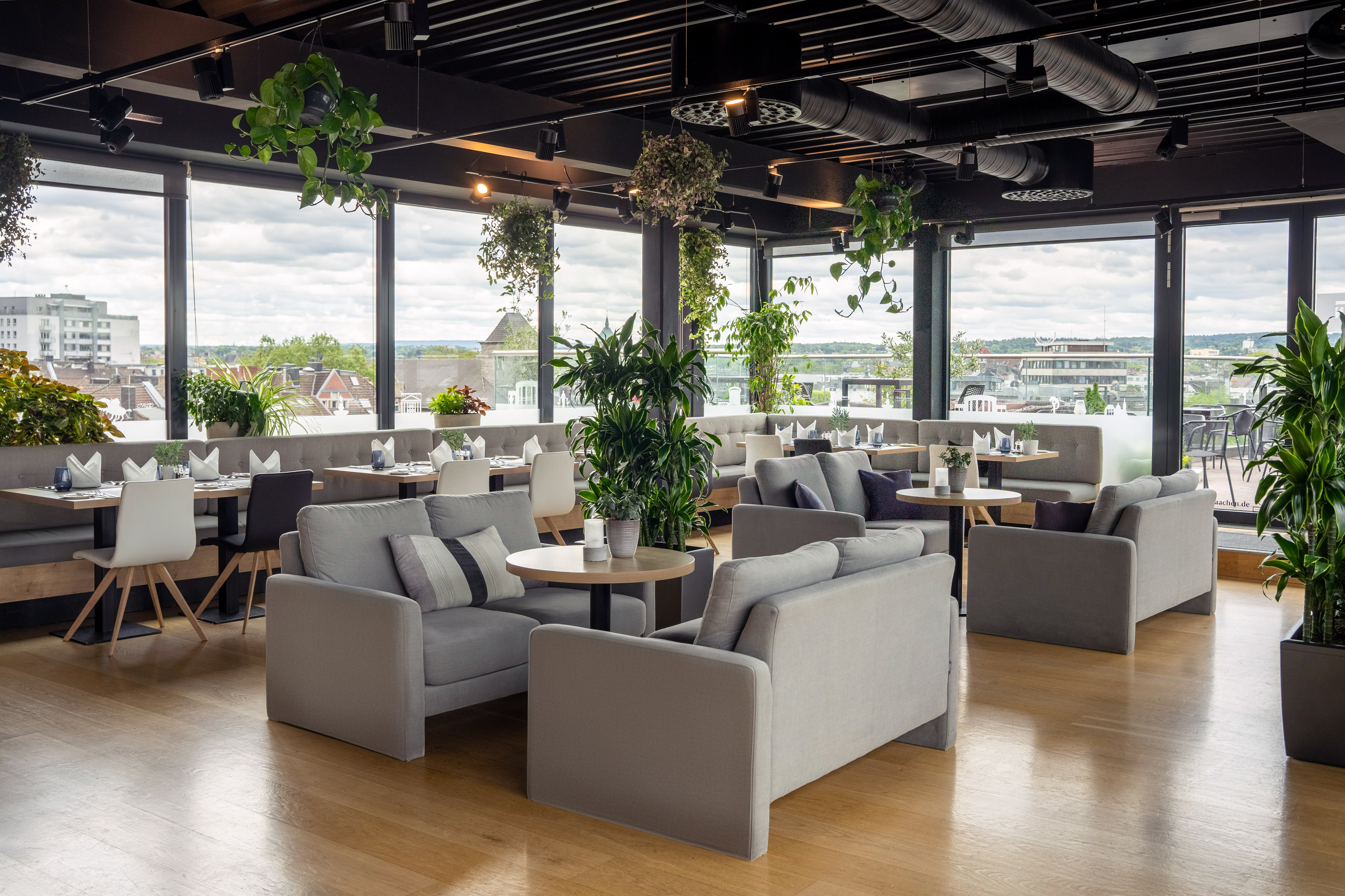 Modern rooftop restaurant lounge with panoramic city views and green plants.