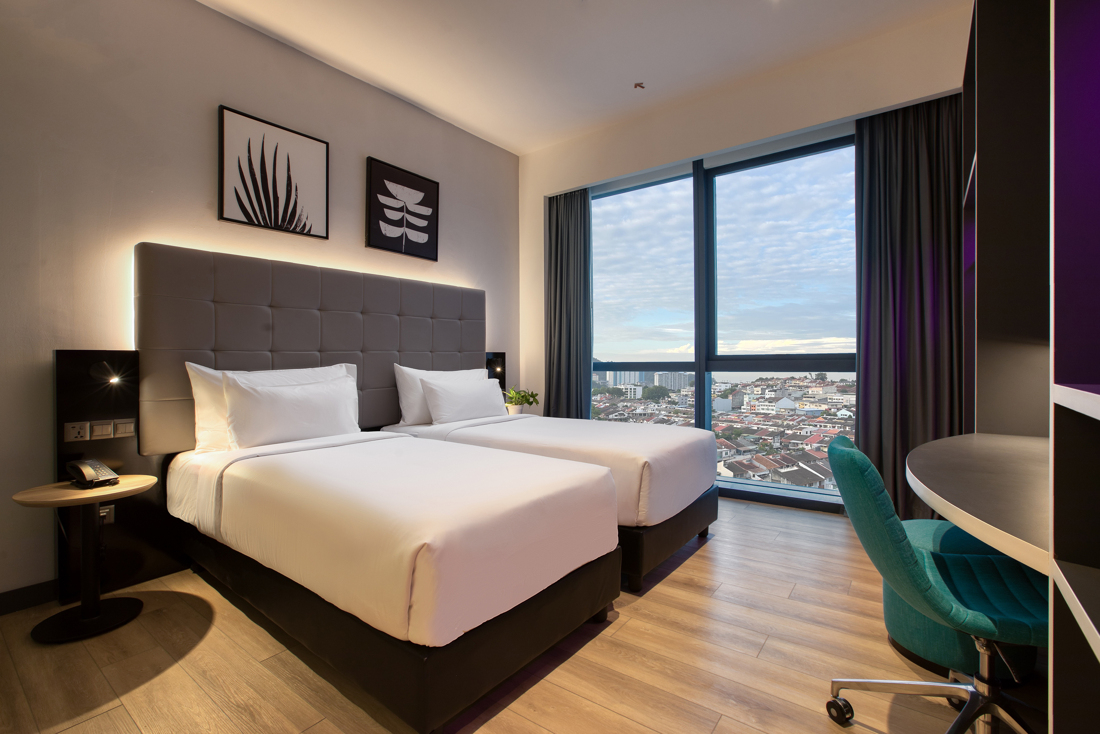Modern hotel room with twin beds, city view, and a teal chair.