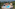 a pool with umbrellas and chairs in front of a body of water