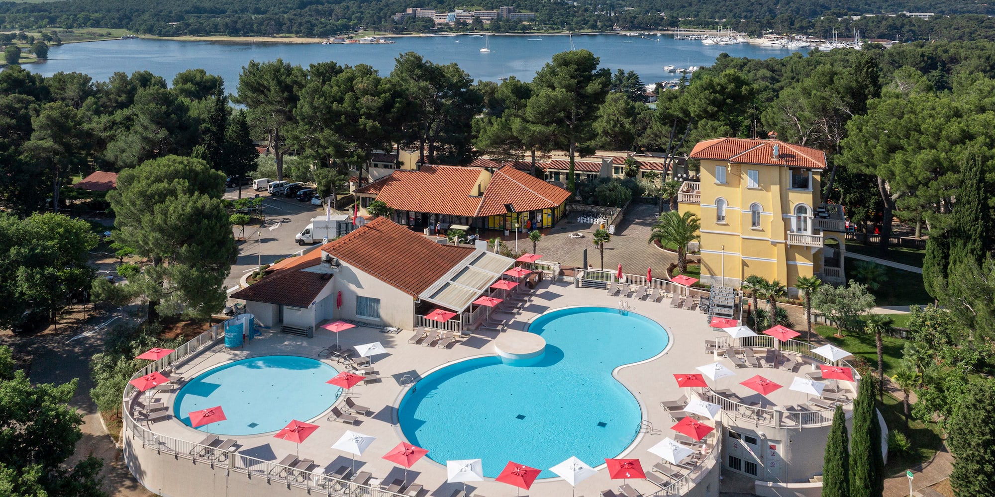 a pool with umbrellas and chairs in front of a body of water