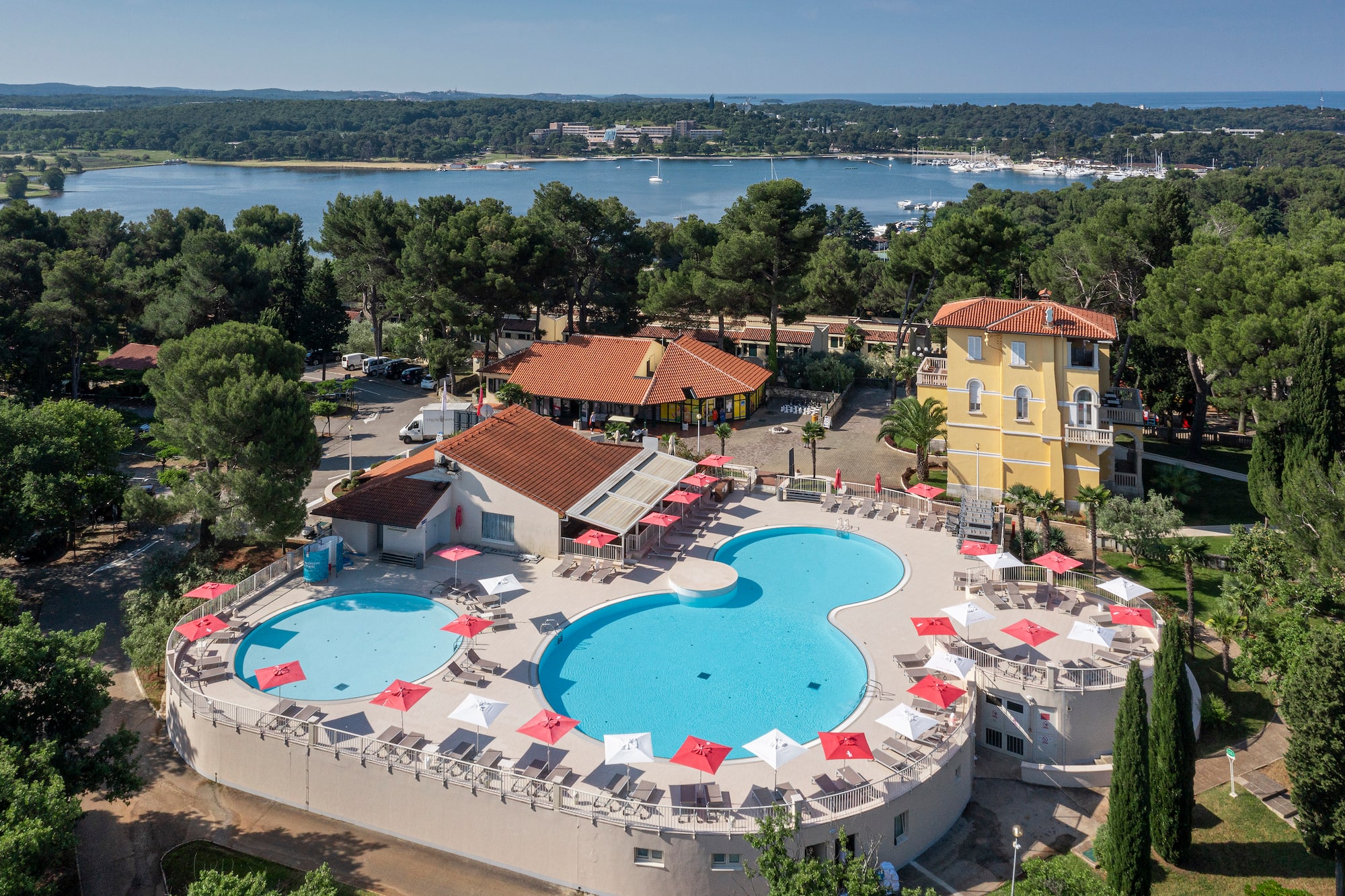 a pool with umbrellas and chairs in front of a body of water