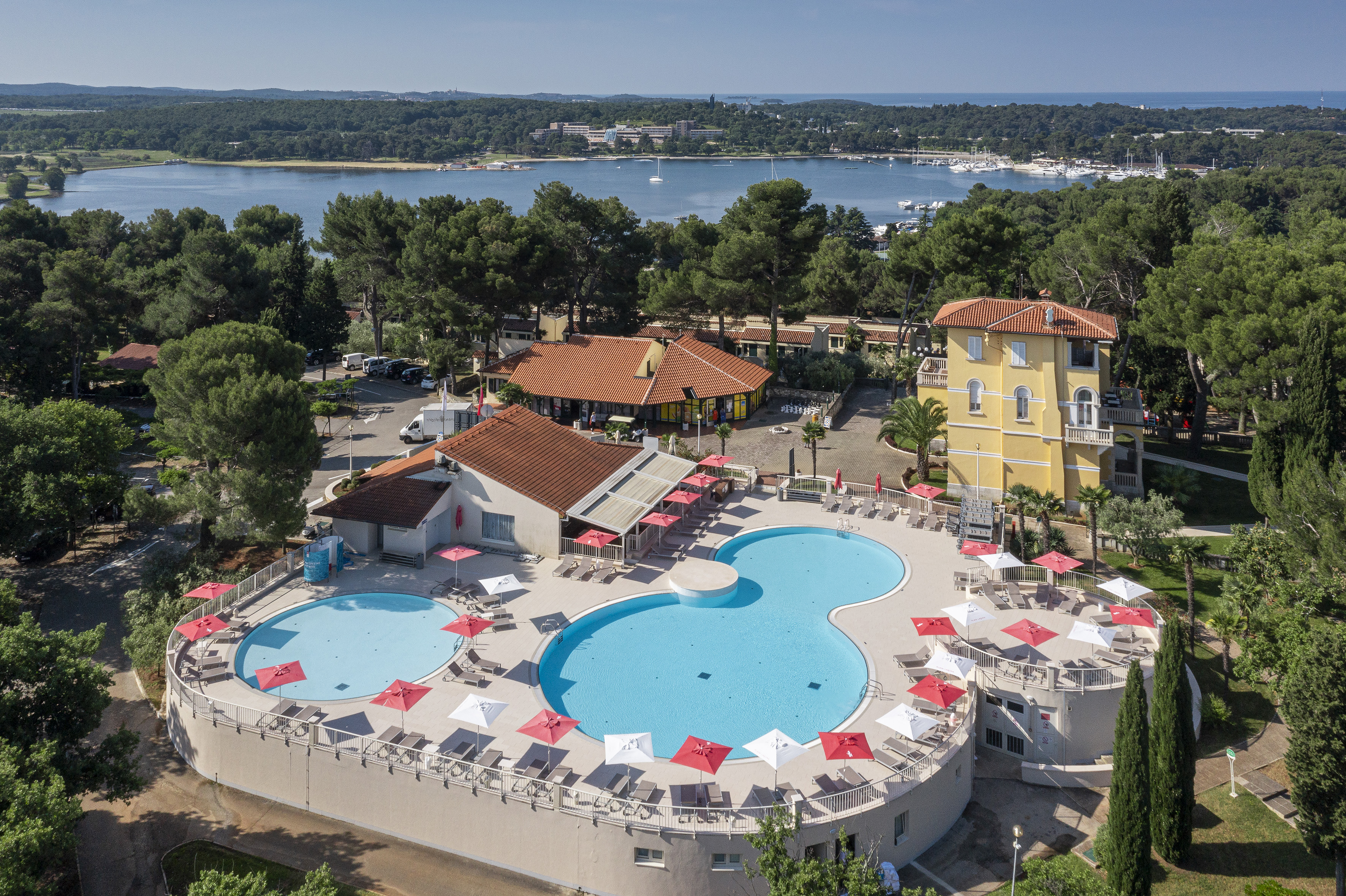 a pool with umbrellas and chairs in front of a body of water