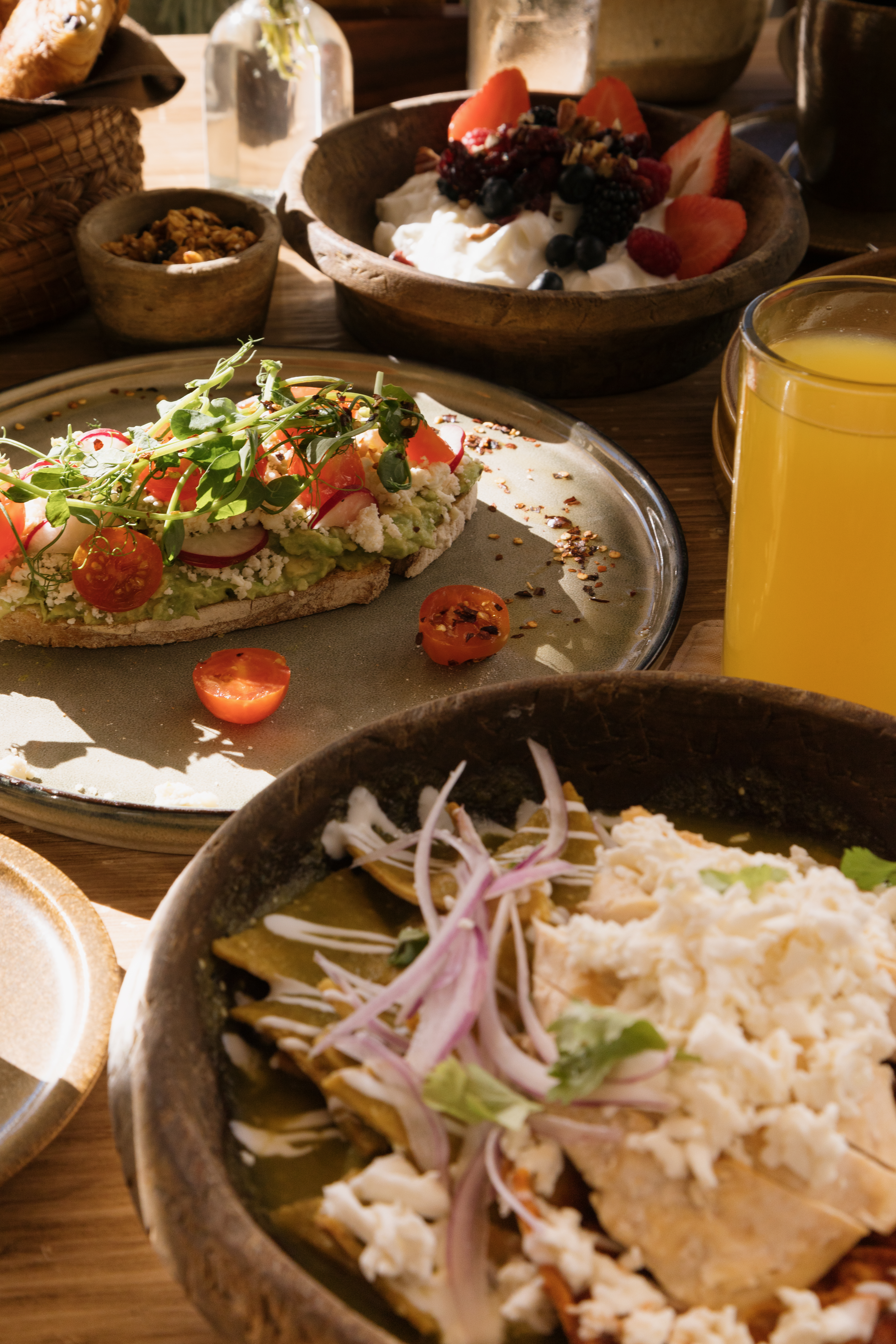 Brunch table with avocado toast, chilaquiles, berry yogurt, and orange juice.