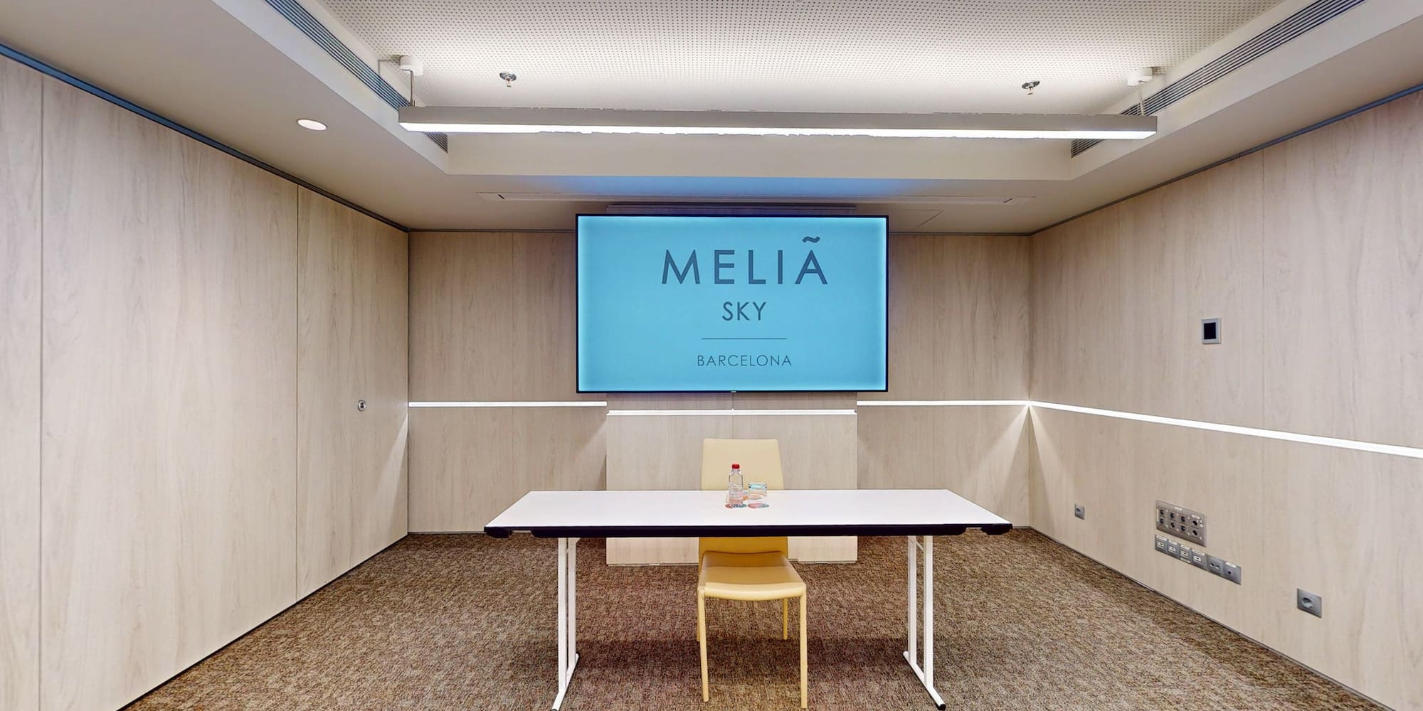 Modern Meliã Sky Barcelona meeting room with large screen, table, and wood walls.
