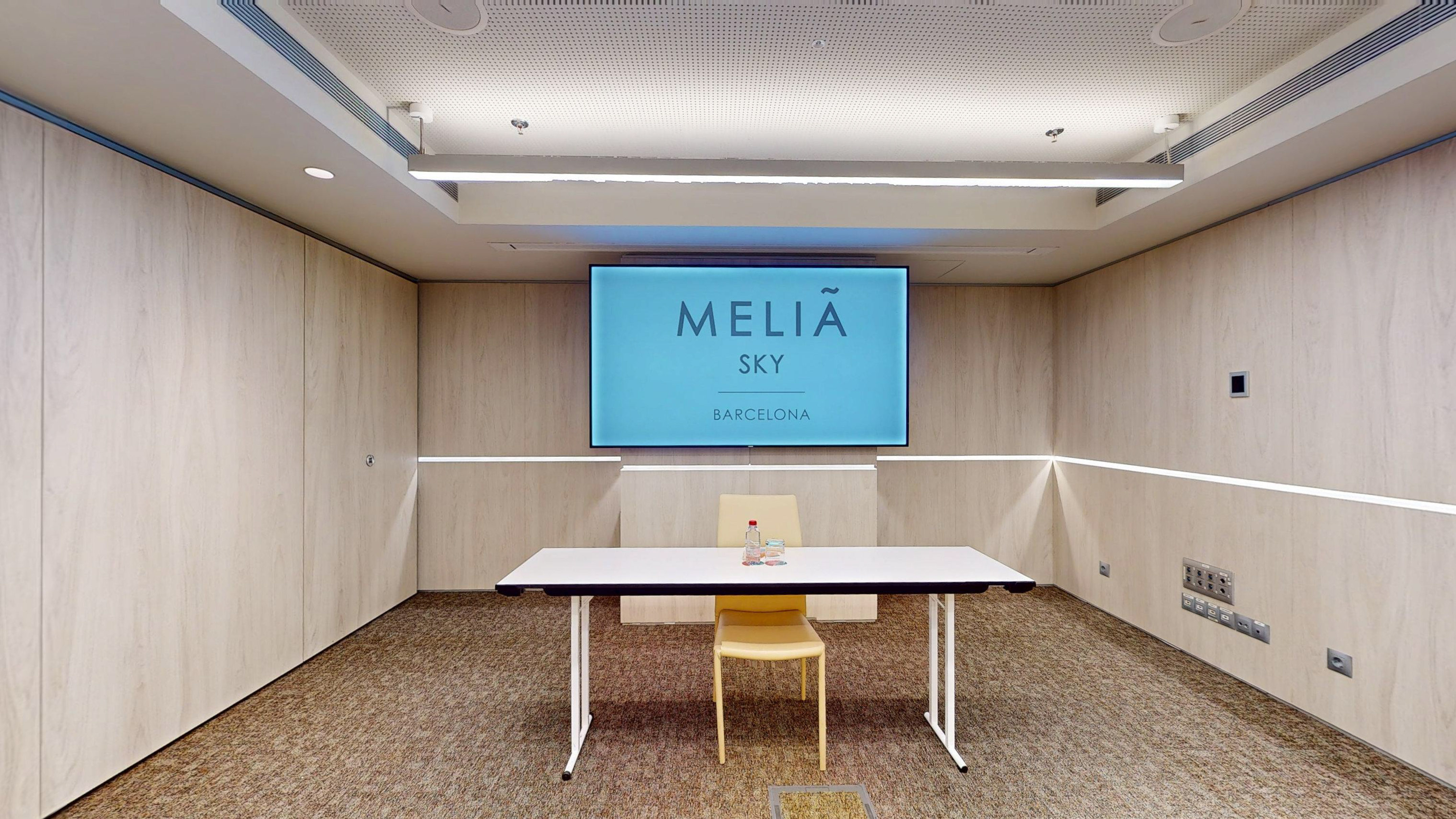 Modern Meliã Sky Barcelona meeting room with large screen, table, and wood walls.