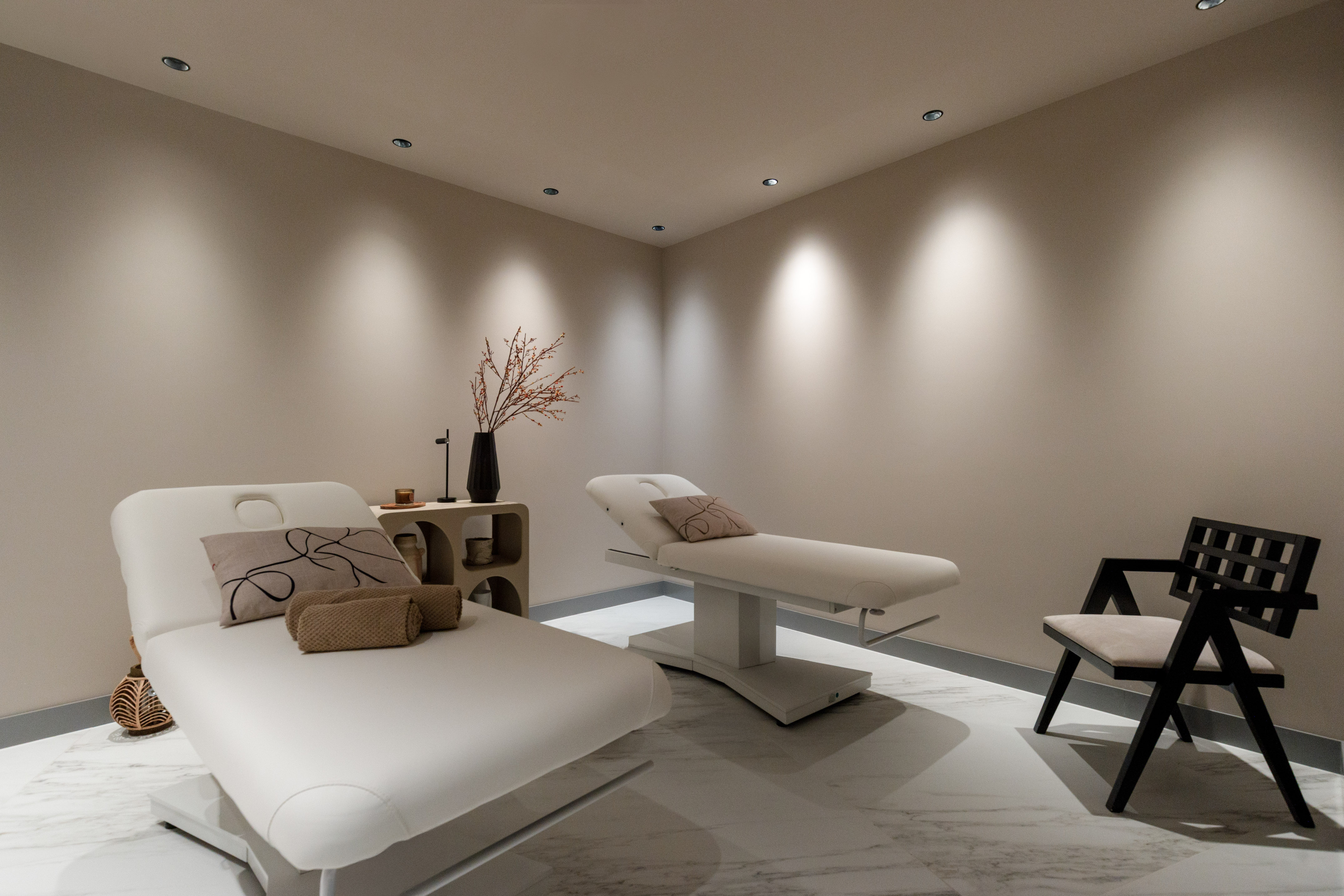 Minimalist spa massage room with two white therapy beds and soft lighting.