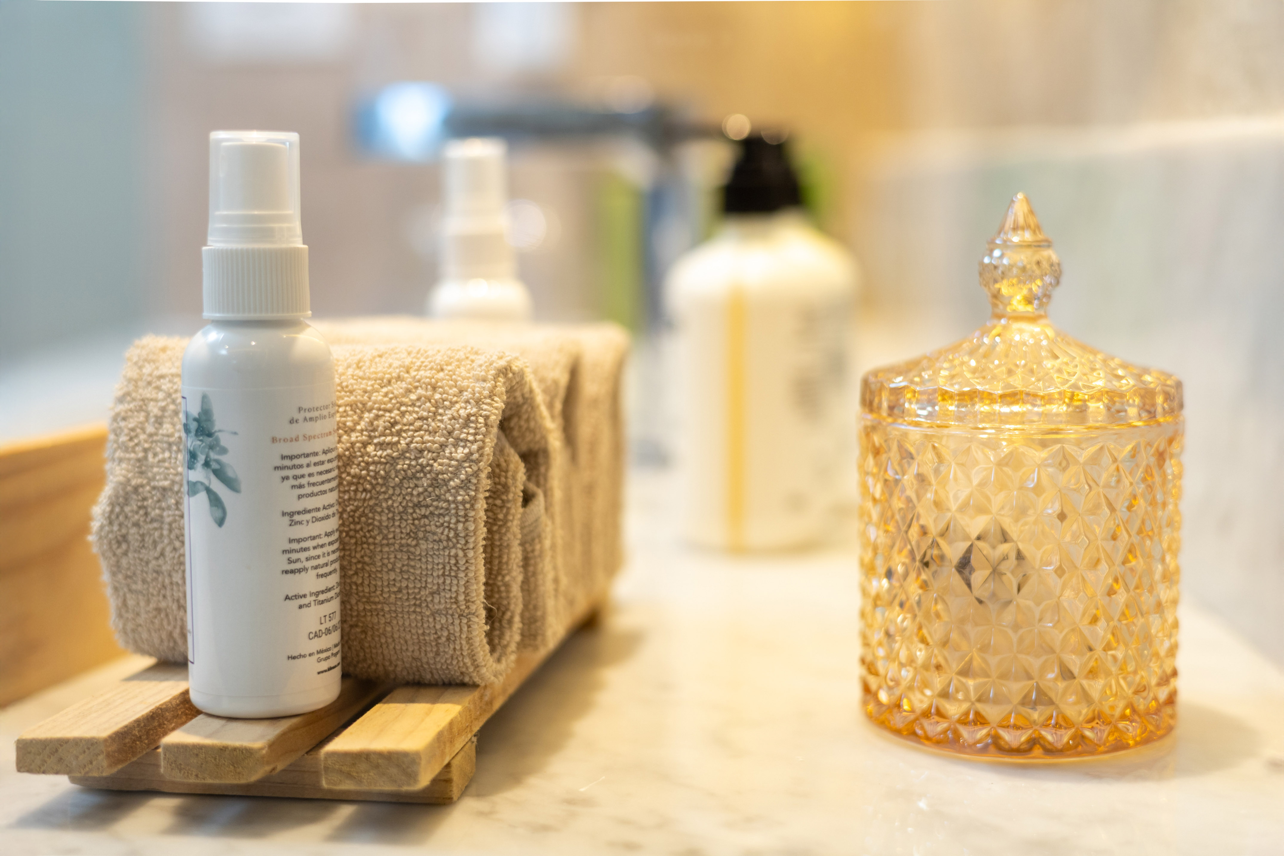 Bathroom toiletries set: broad spectrum spray, towels, amber jar on marble.