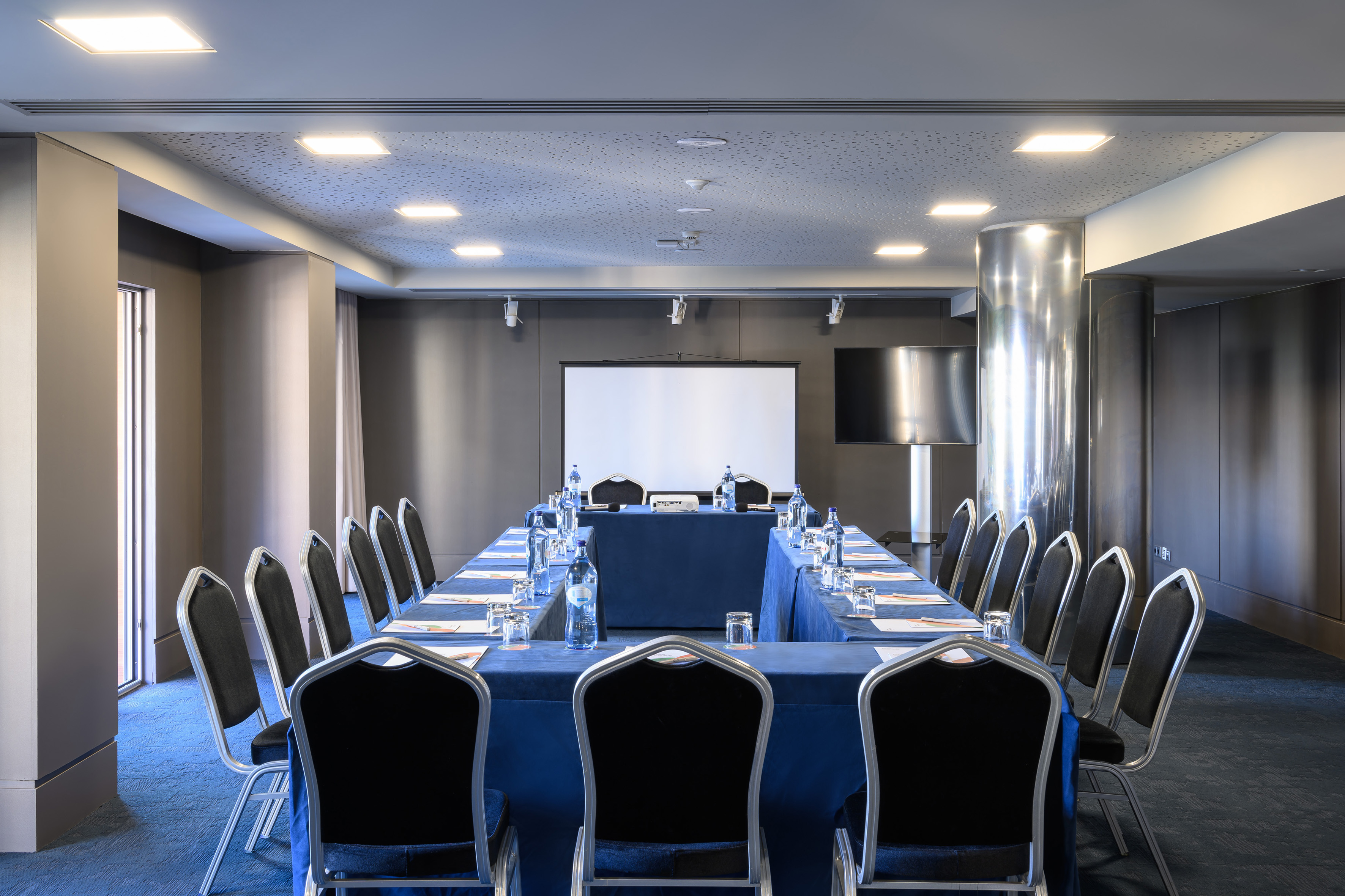 Modern U-shape conference room with blue tables, chairs, and projector screen.