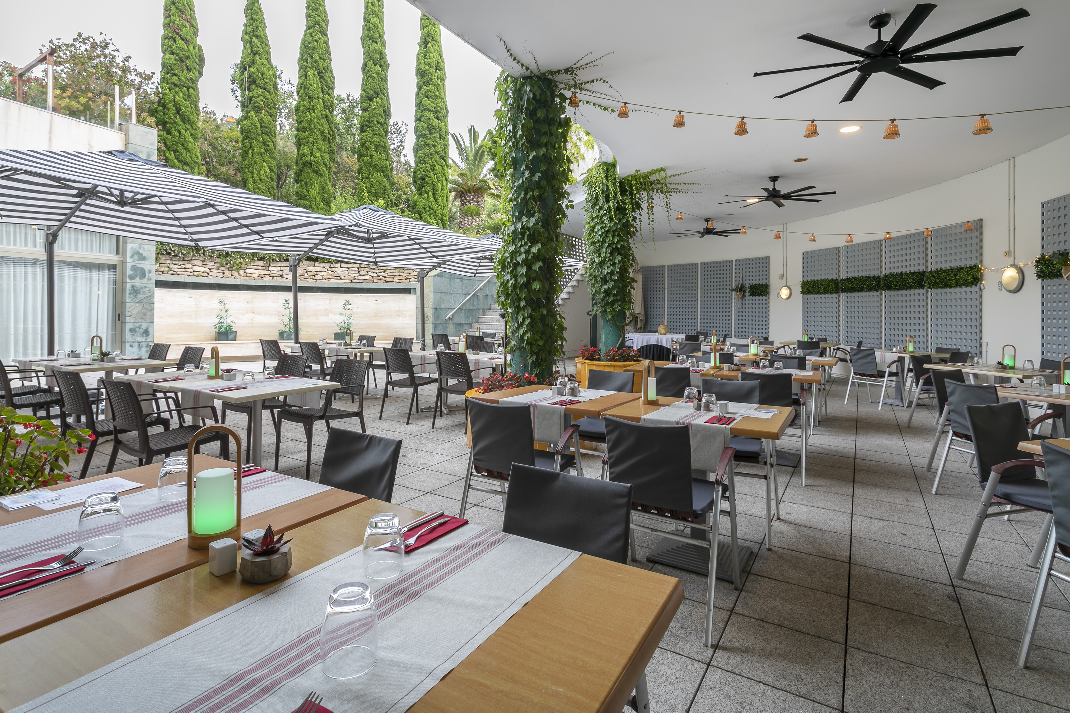 Modern outdoor restaurant patio with dining tables, striped umbrellas, and ivy.
