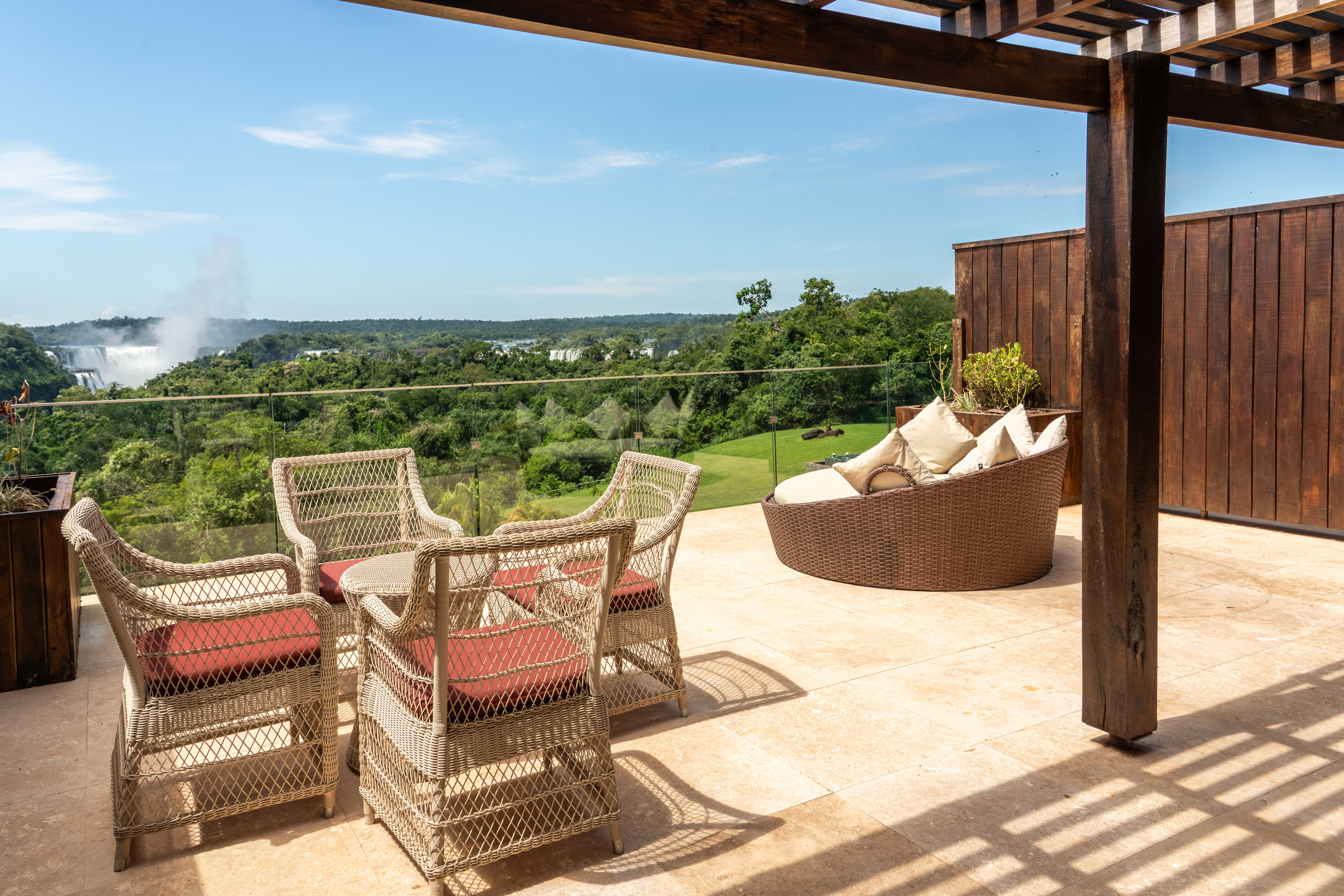 Wicker patio furniture under pergola, panoramic view of Iguazu Falls.