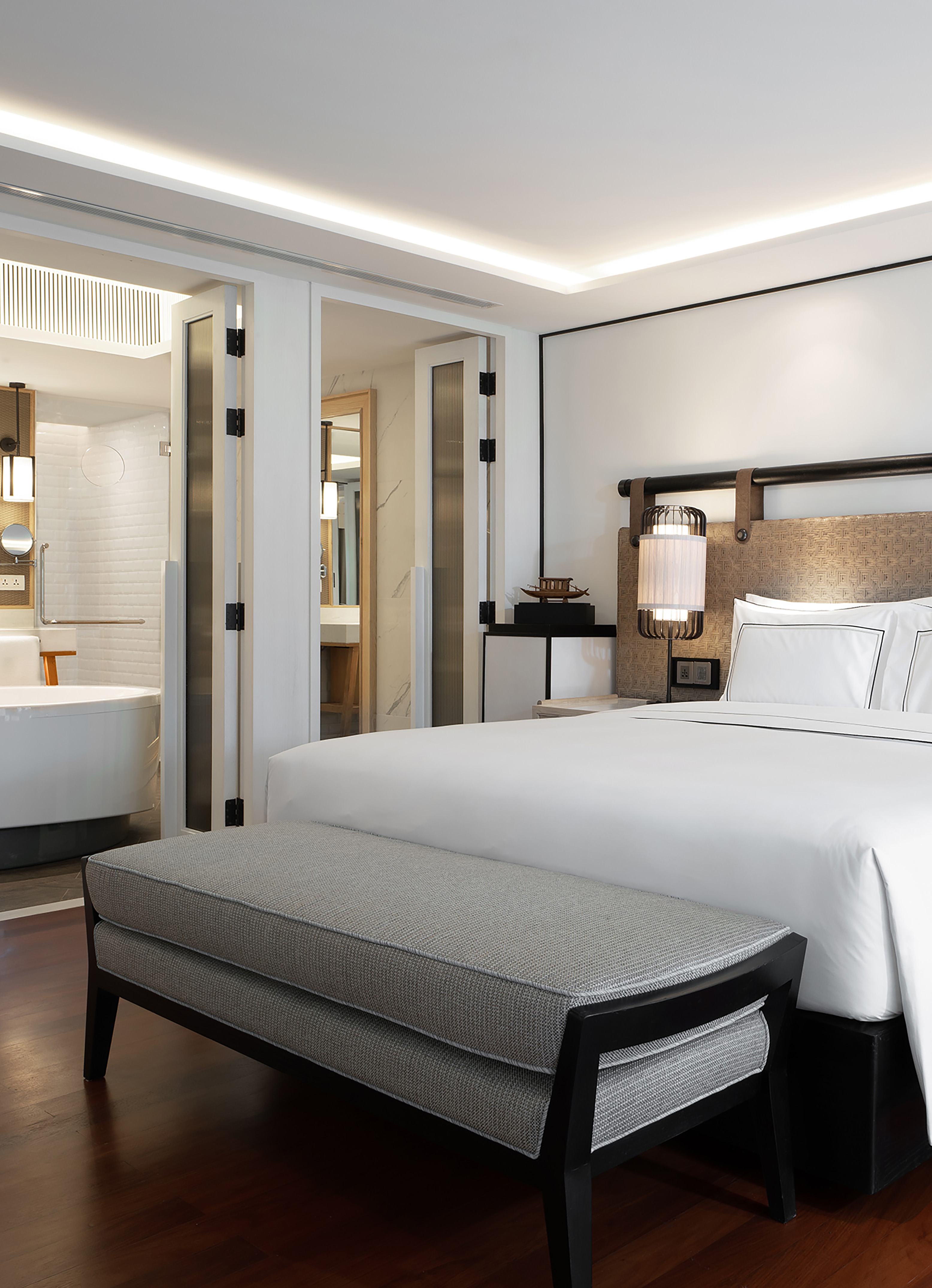 Elegant hotel suite with spacious king bed, bench, and adjoining bathroom.