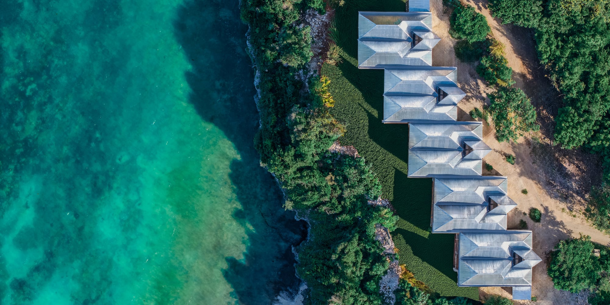 Aerial: Coastal resort villas by turquoise ocean and lush greenery.
