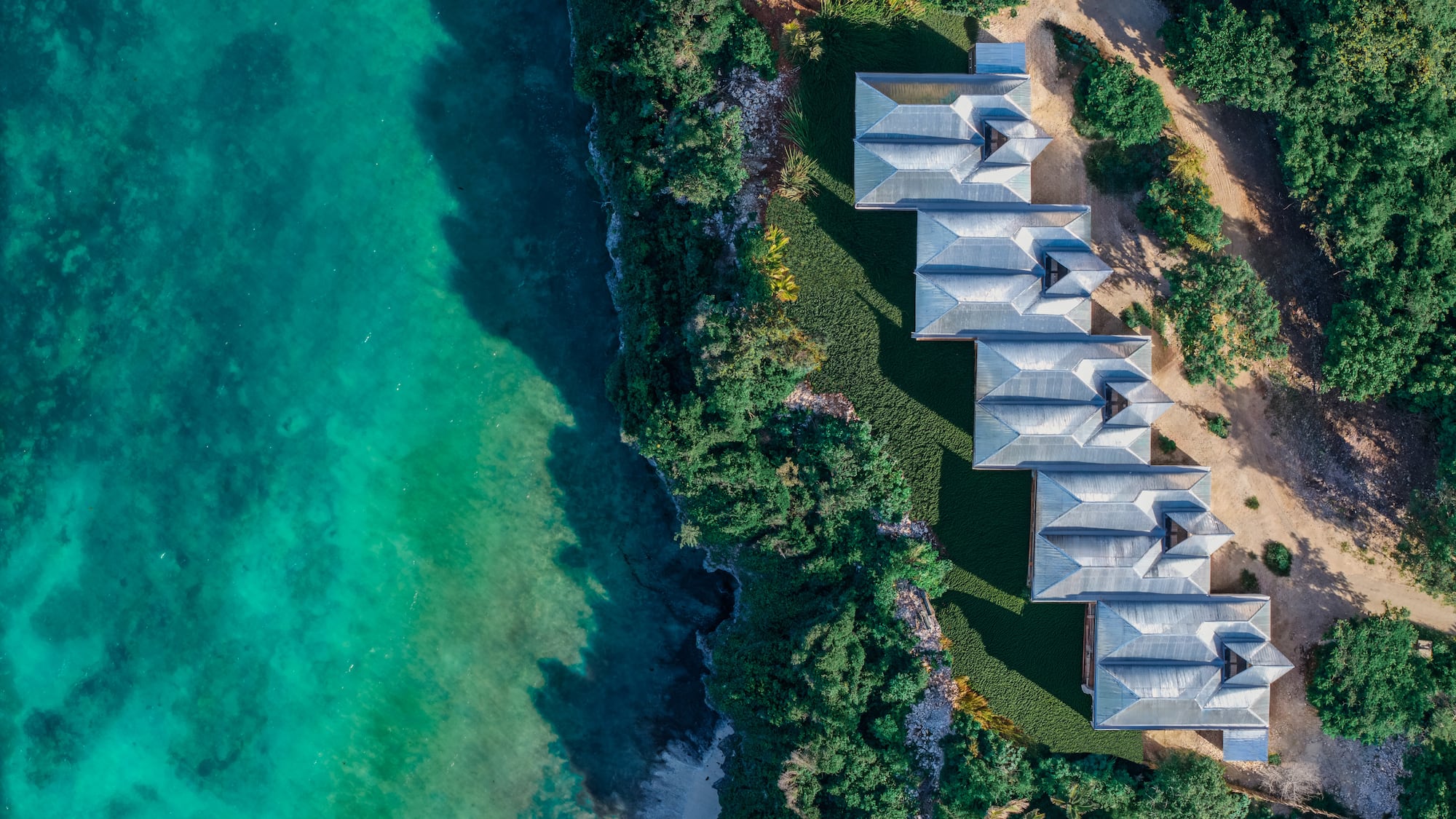 Aerial: Coastal resort villas by turquoise ocean and lush greenery.