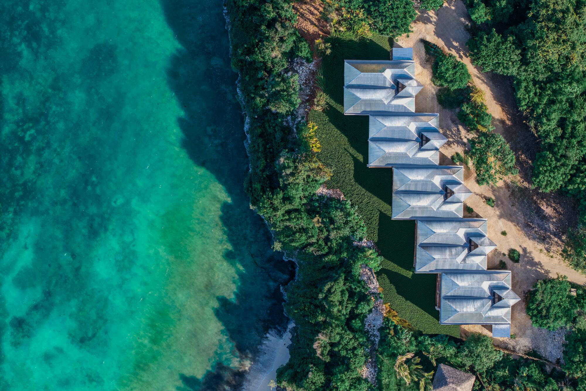 Aerial: Coastal resort villas by turquoise ocean and lush greenery.