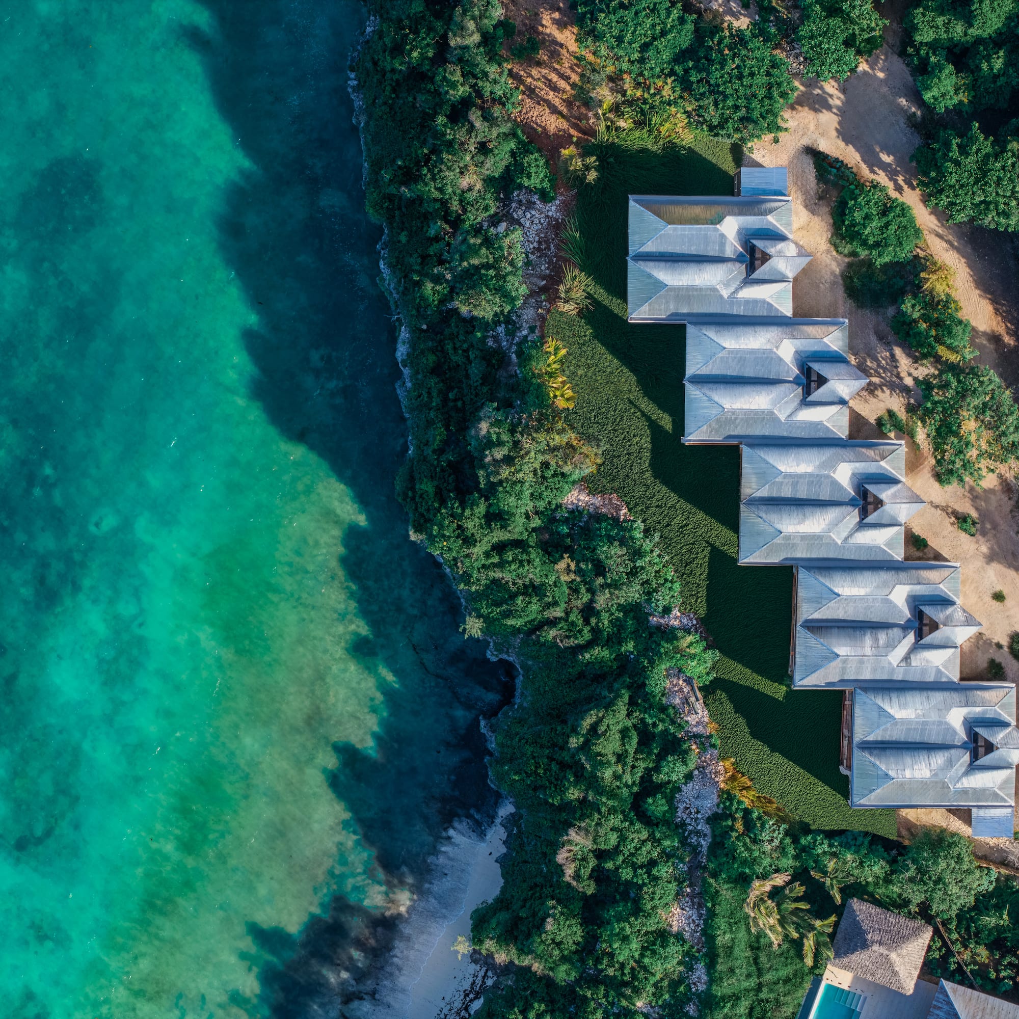 Aerial: Coastal resort villas by turquoise ocean and lush greenery.