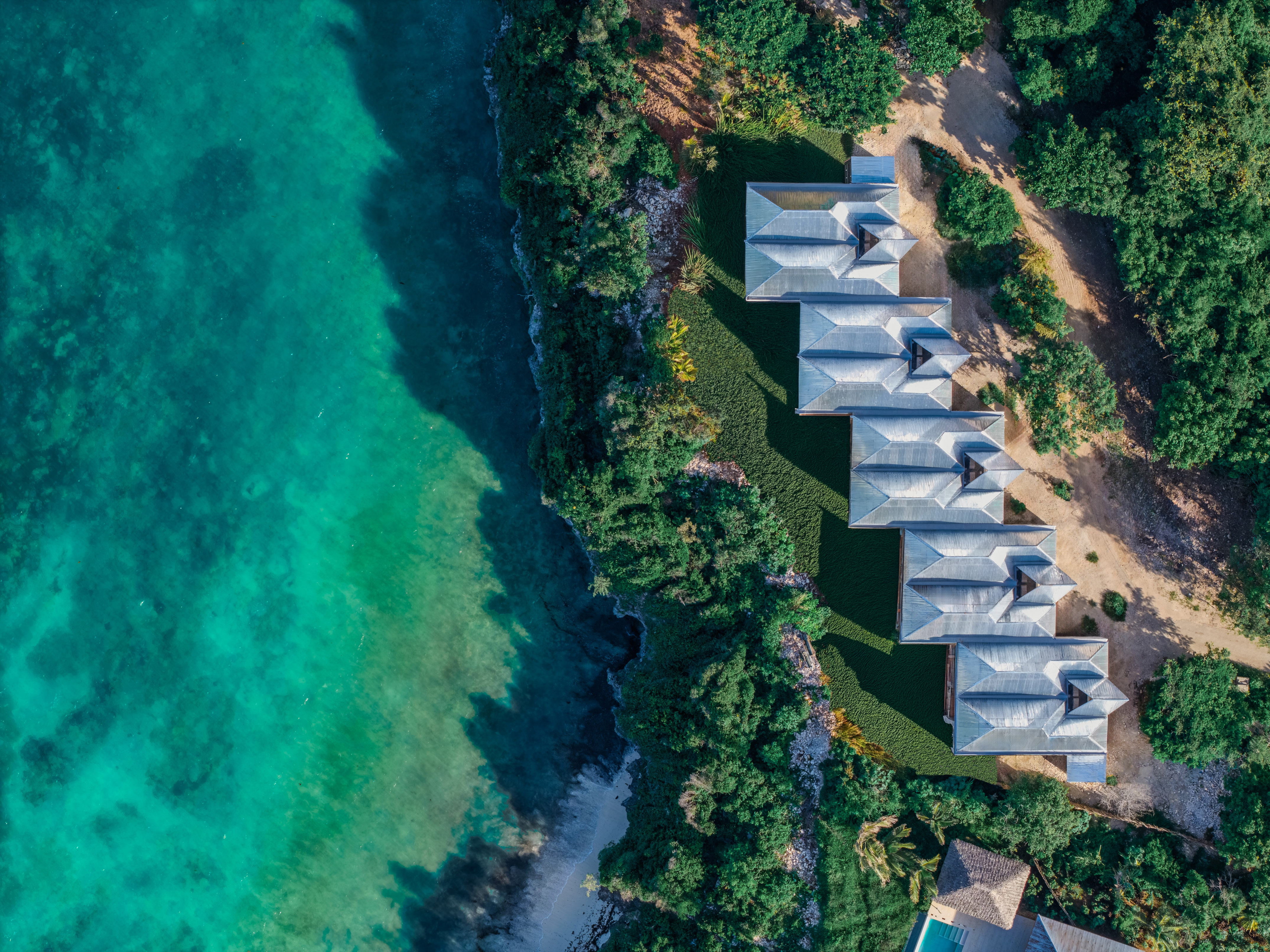 Aerial: Coastal resort villas by turquoise ocean and lush greenery.
