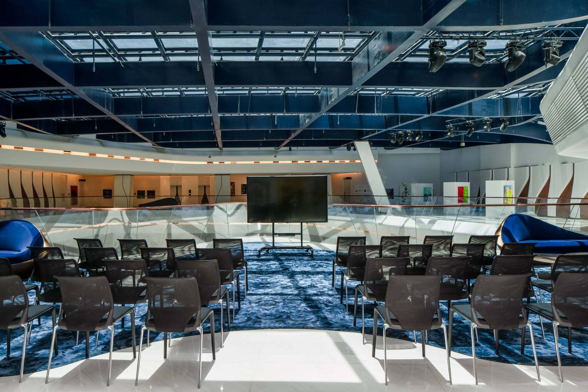 Modern presentation room with black chairs, large screen, and skylights.