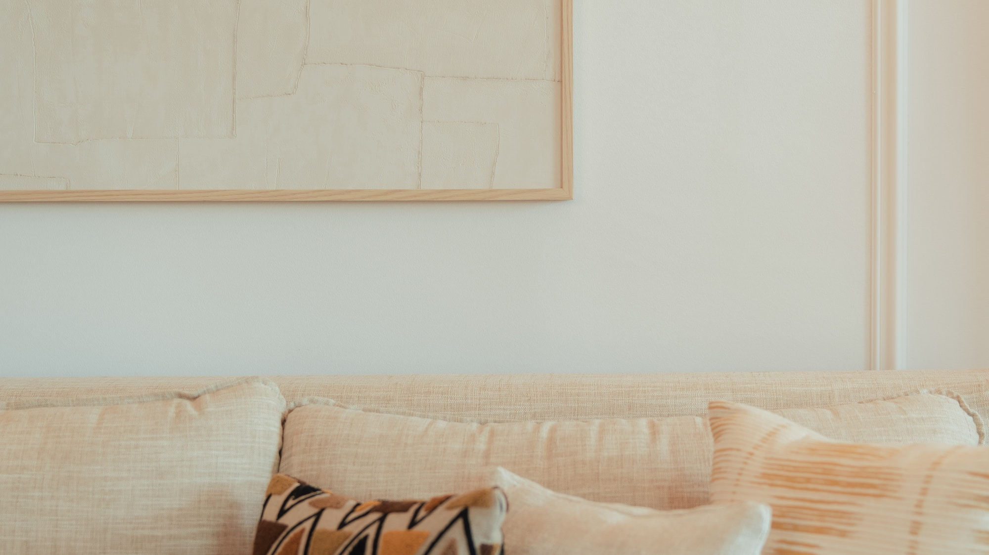 Cream sofa with geometric and textured pillows, framed neutral abstract art.