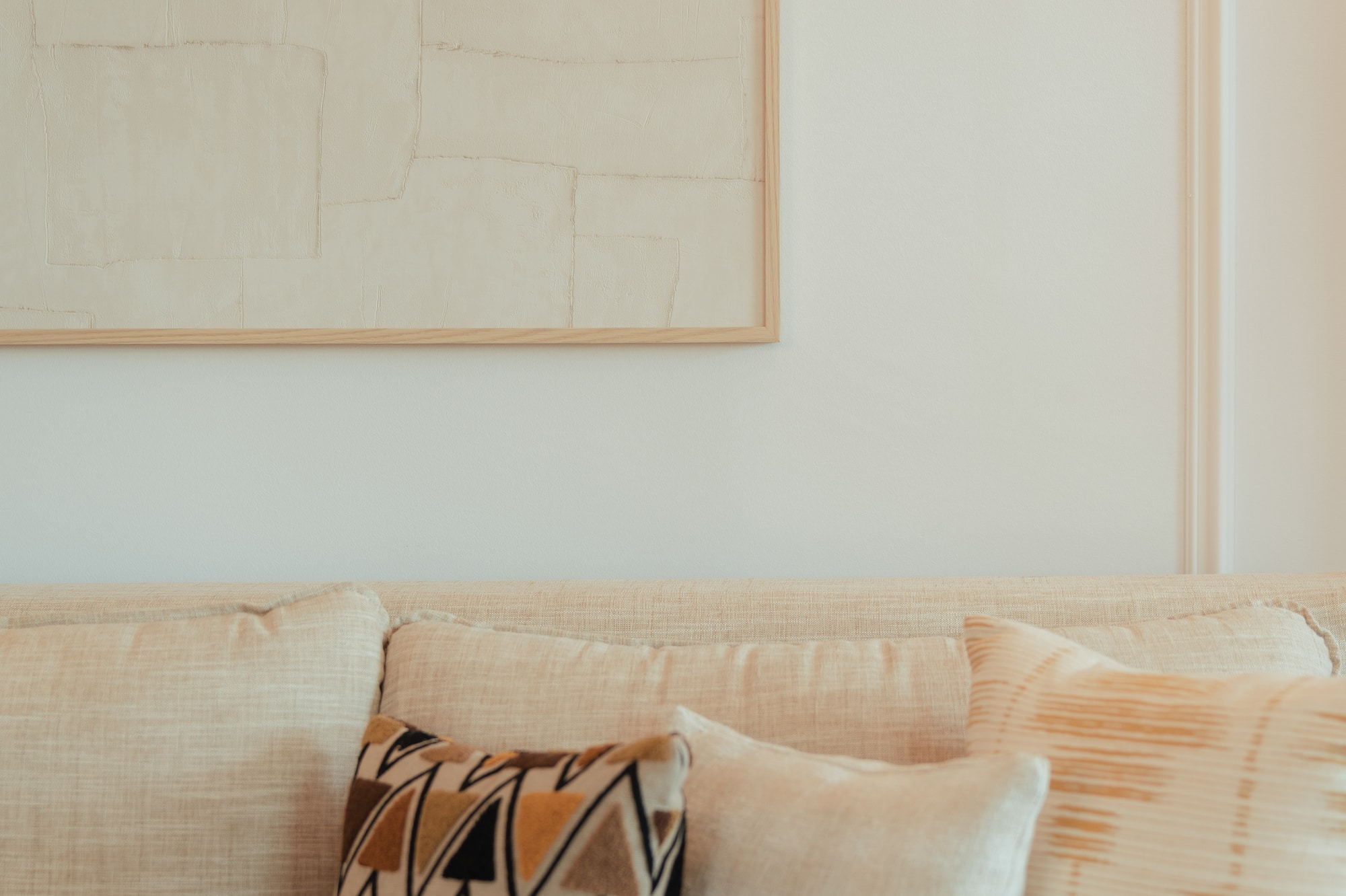 Cream sofa with geometric and textured pillows, framed neutral abstract art.