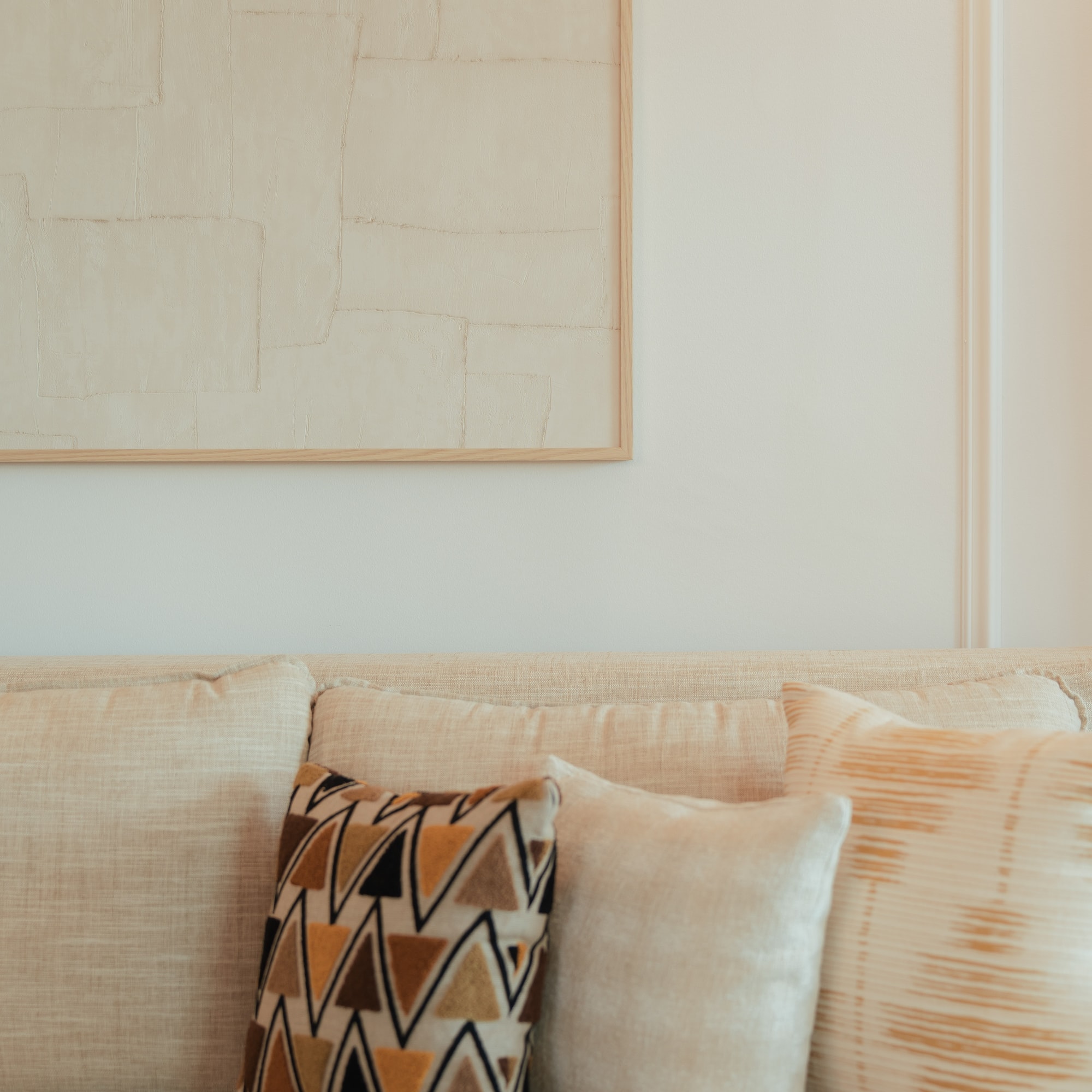 Cream sofa with geometric and textured pillows, framed neutral abstract art.