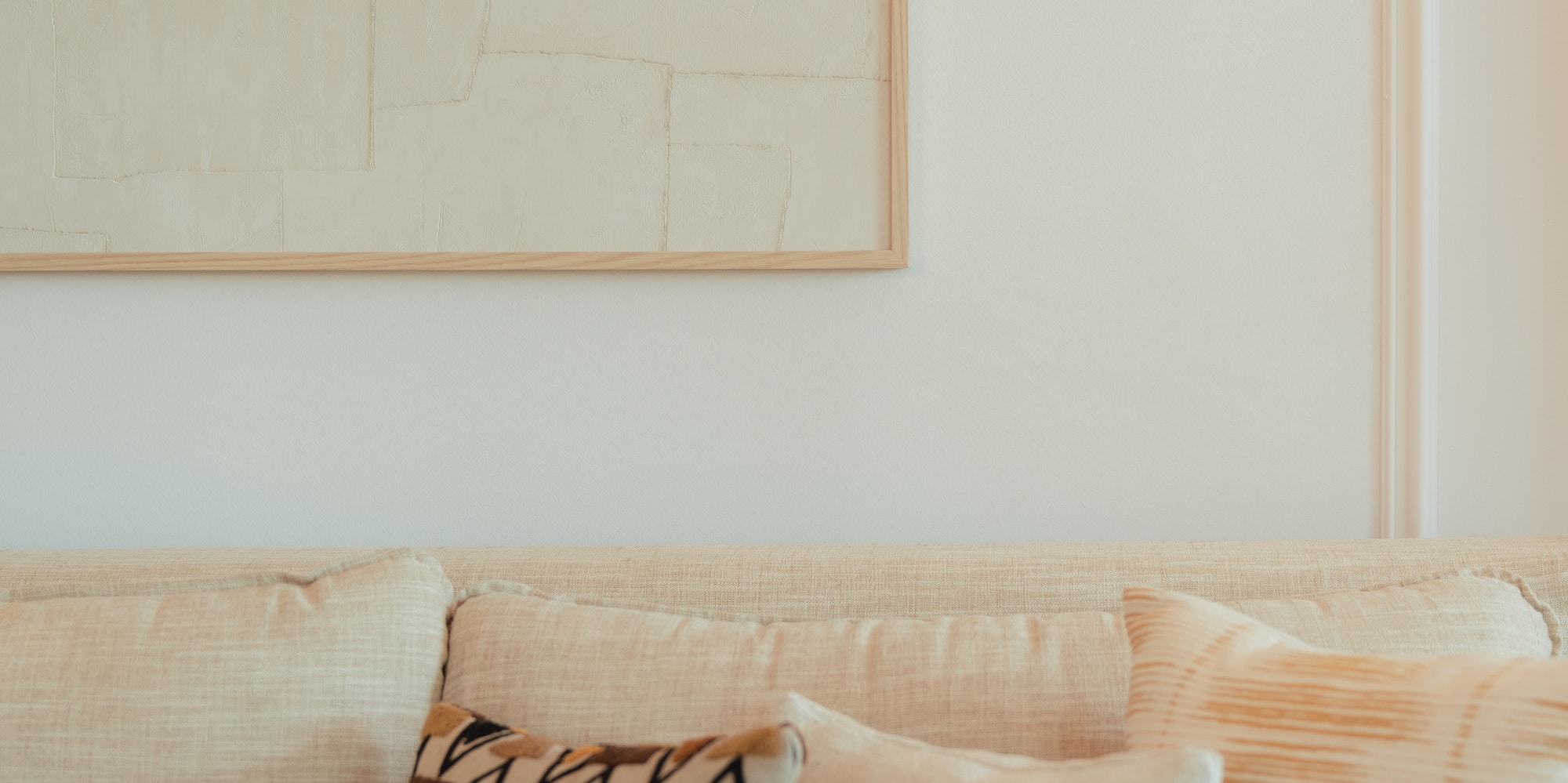 Cream sofa with geometric and textured pillows, framed neutral abstract art.