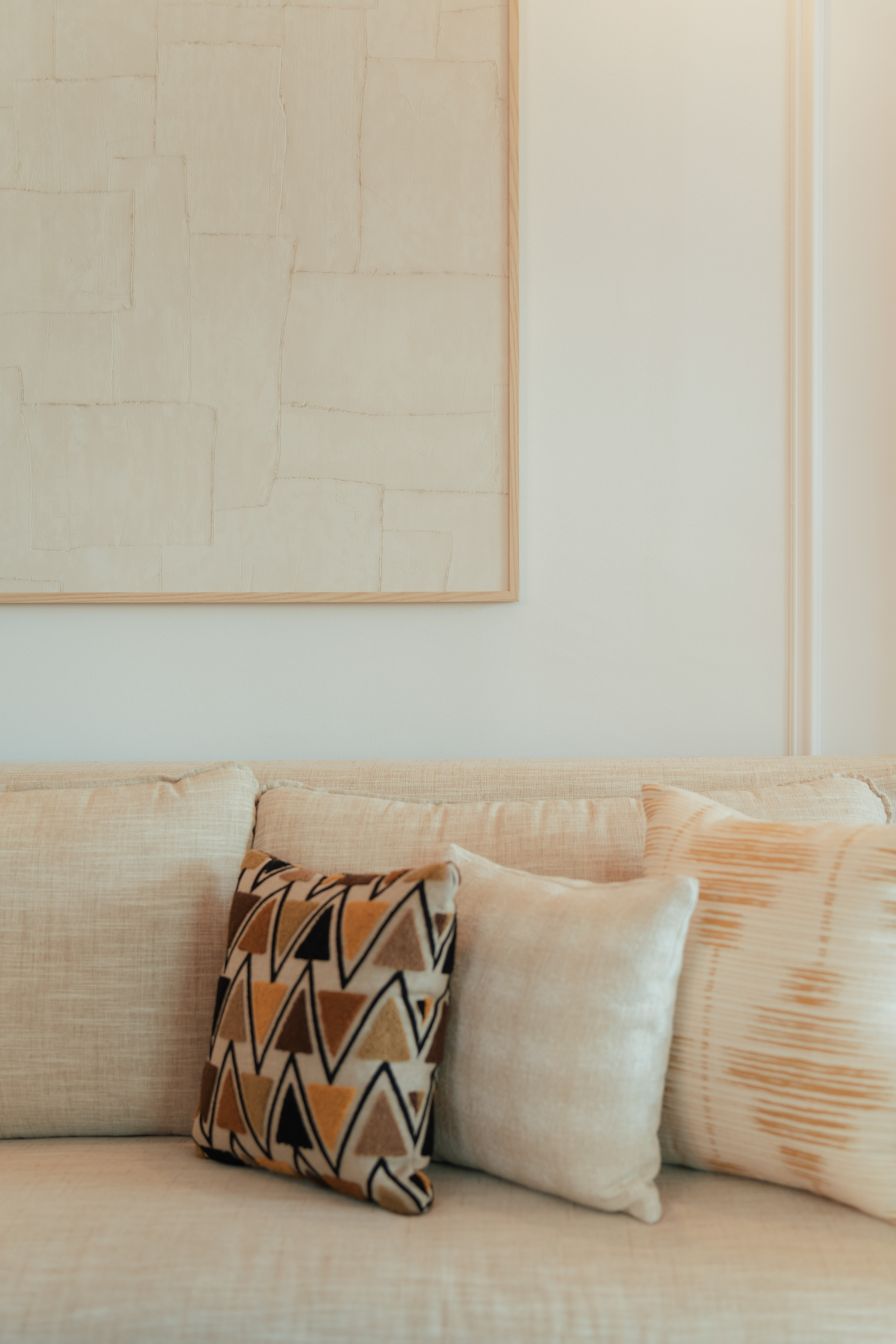Cream sofa with geometric and textured pillows, framed neutral abstract art.