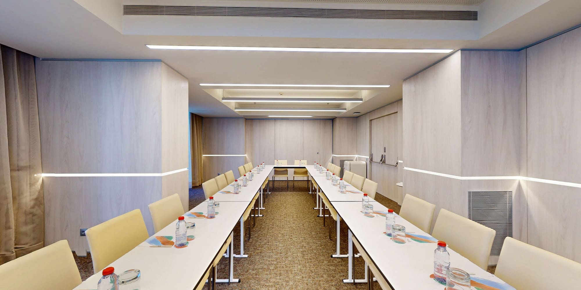 Modern U-shape conference room with tables, light chairs, and bright LED lighting.