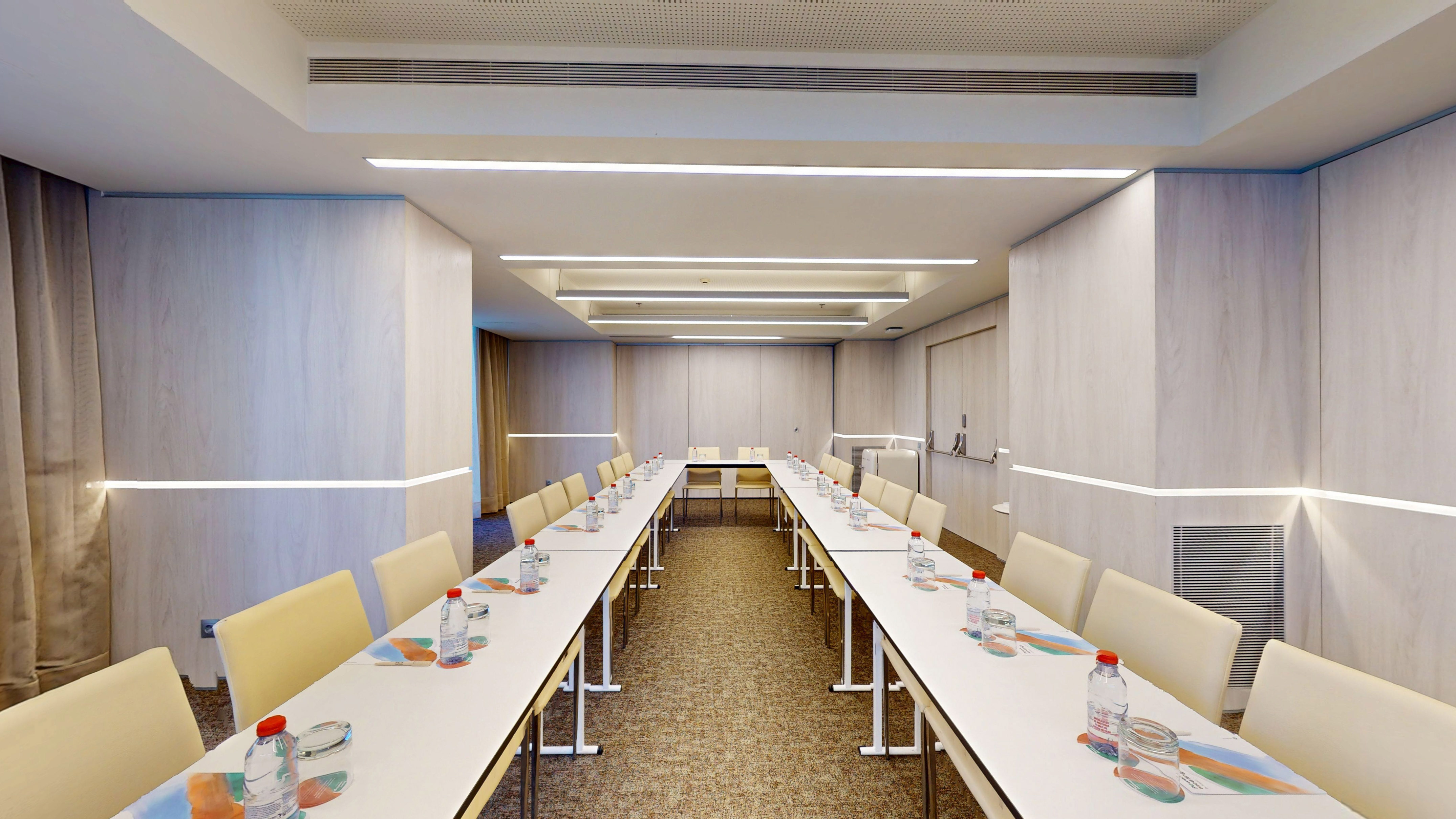 Modern U-shape conference room with tables, light chairs, and bright LED lighting.