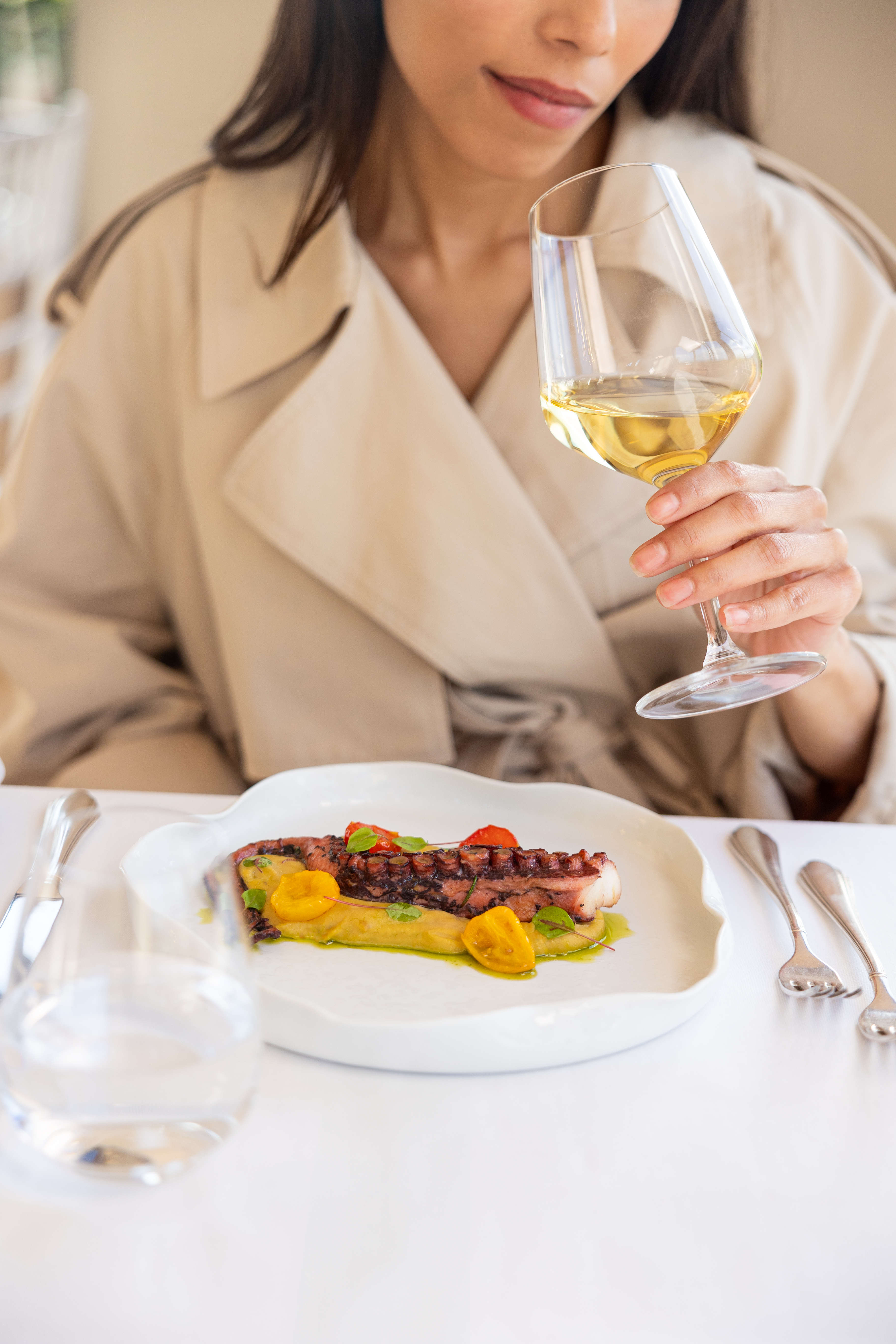 Woman holds white wine, grilled octopus plate, fine dining.