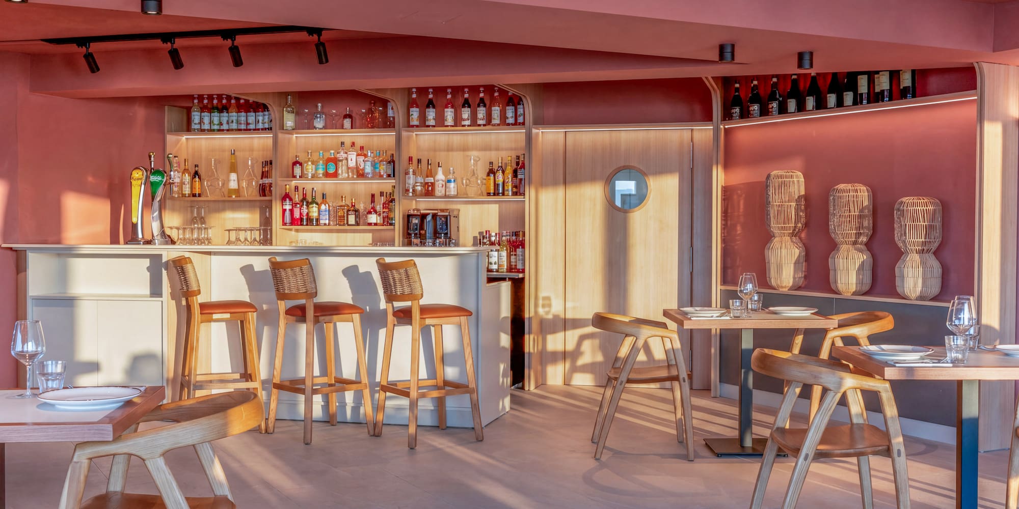 Modern pink bar and restaurant with wooden chairs and liquor display.