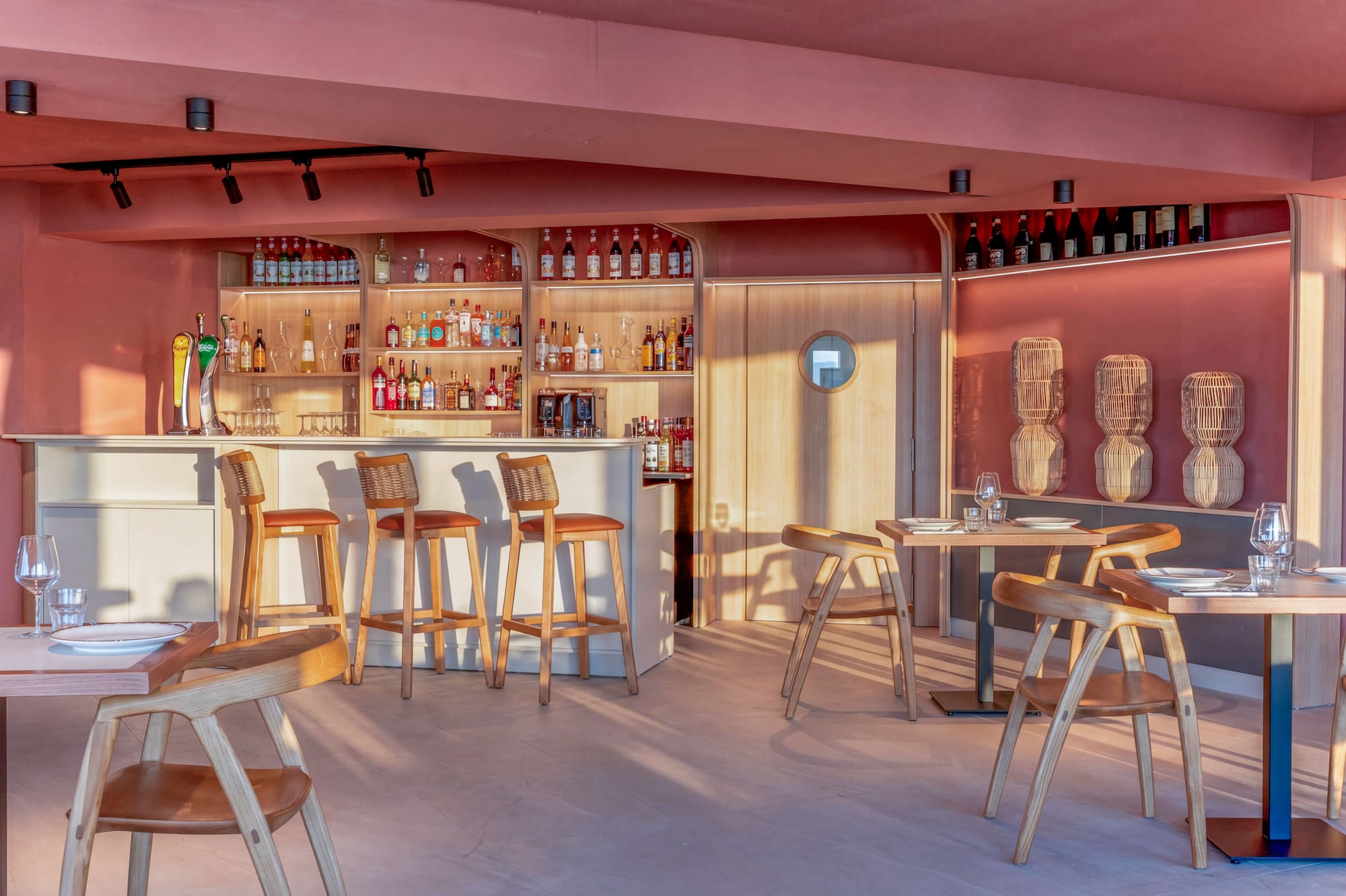 Modern pink bar and restaurant with wooden chairs and liquor display.