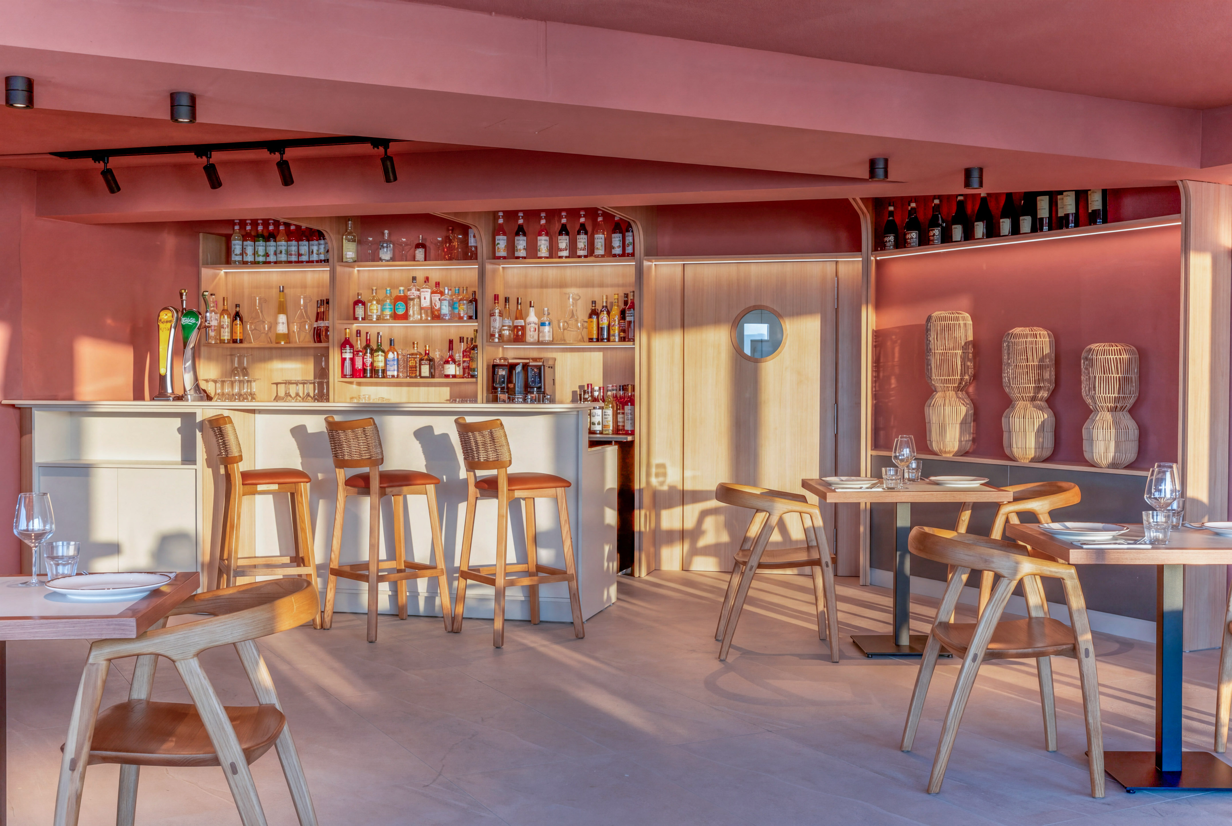 Modern pink bar and restaurant with wooden chairs and liquor display.
