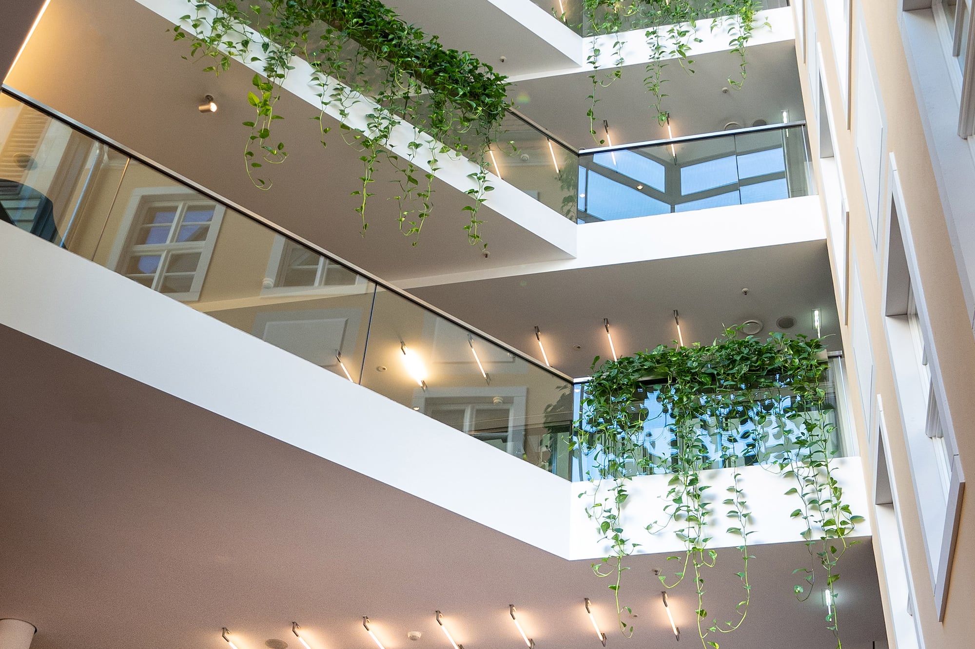 Modern multi-level atrium with glass balconies and cascading green plants.