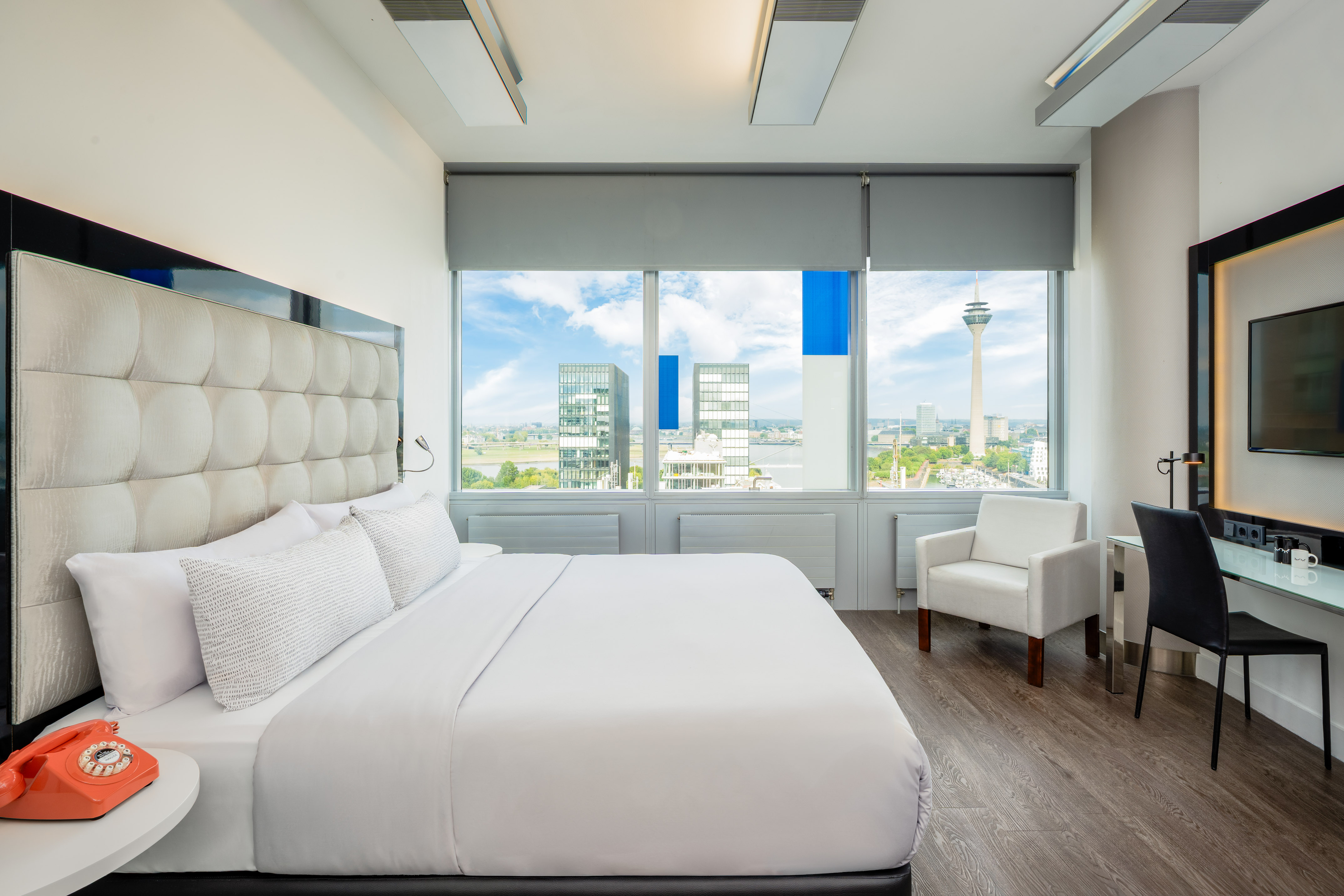Modern hotel room with bed, desk, and city view of Düsseldorf Rheinturm.