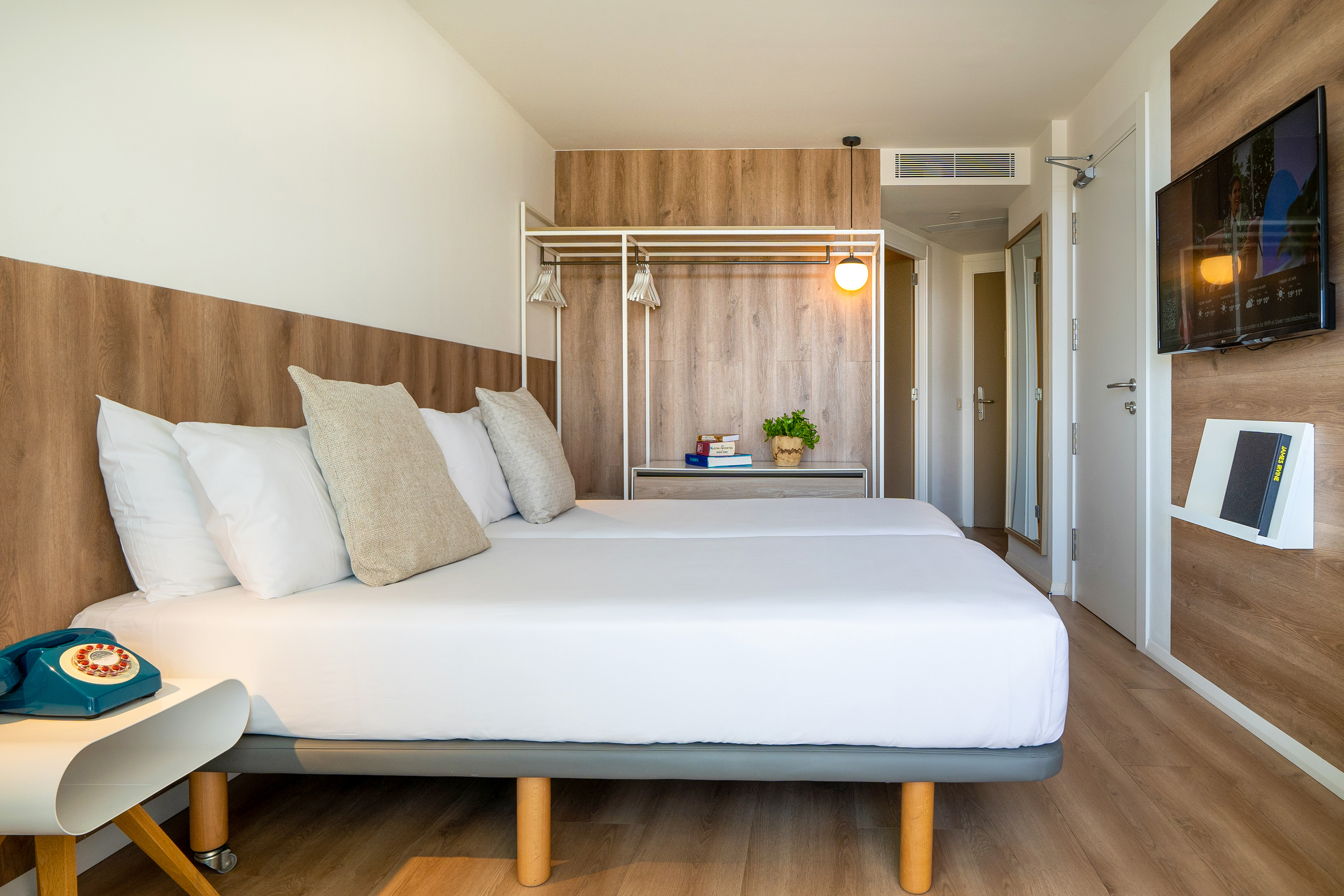 Clean, modern hotel bedroom with twin beds, wood decor, TV, and retro phone.