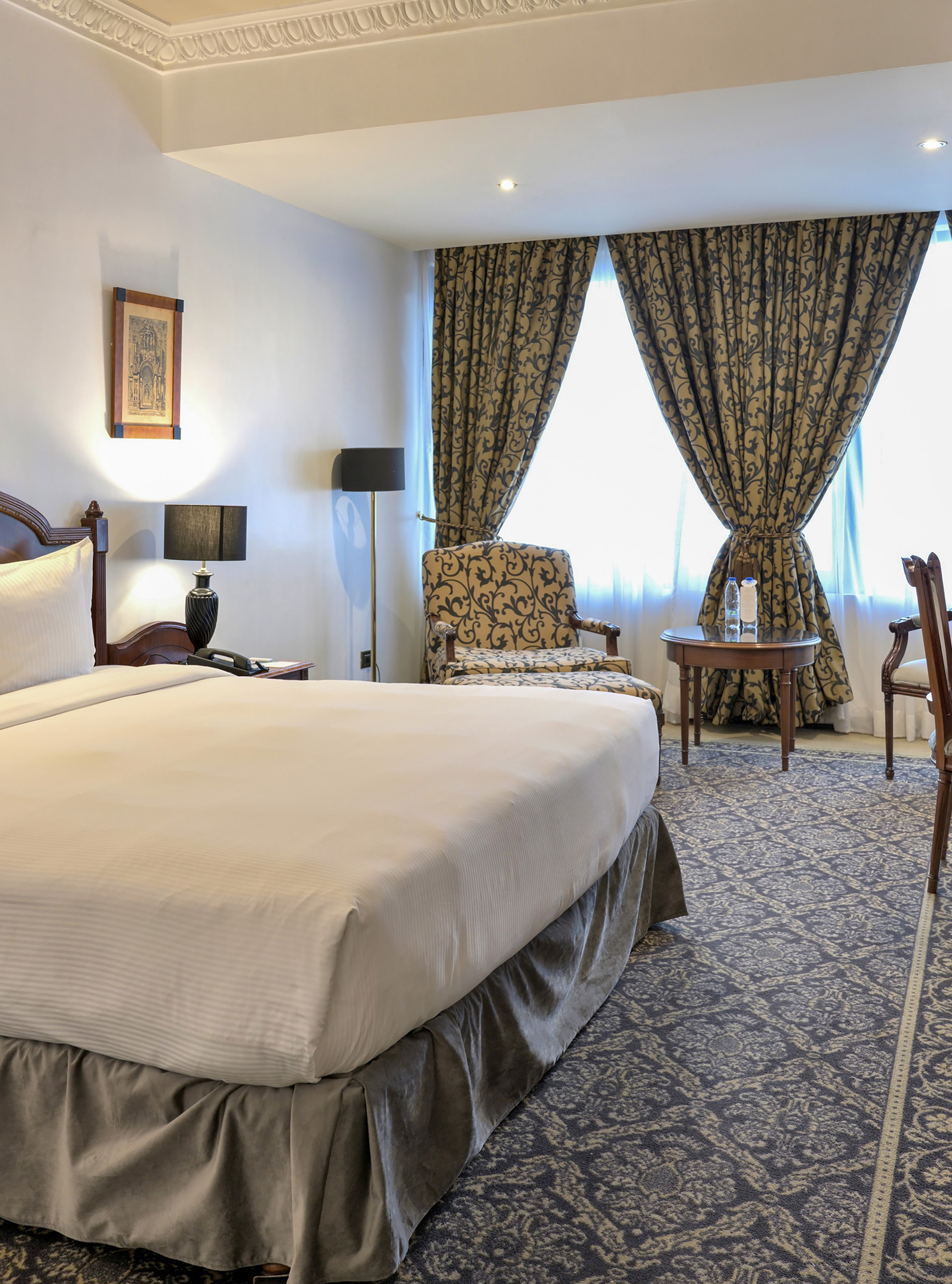 Hotel bedroom with a bed, patterned curtains, armchair, and ornate carpet.