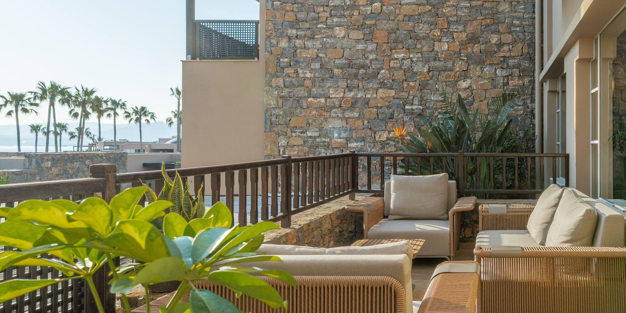 Resort balcony with elegant outdoor seating, stone wall, and tropical sea view.