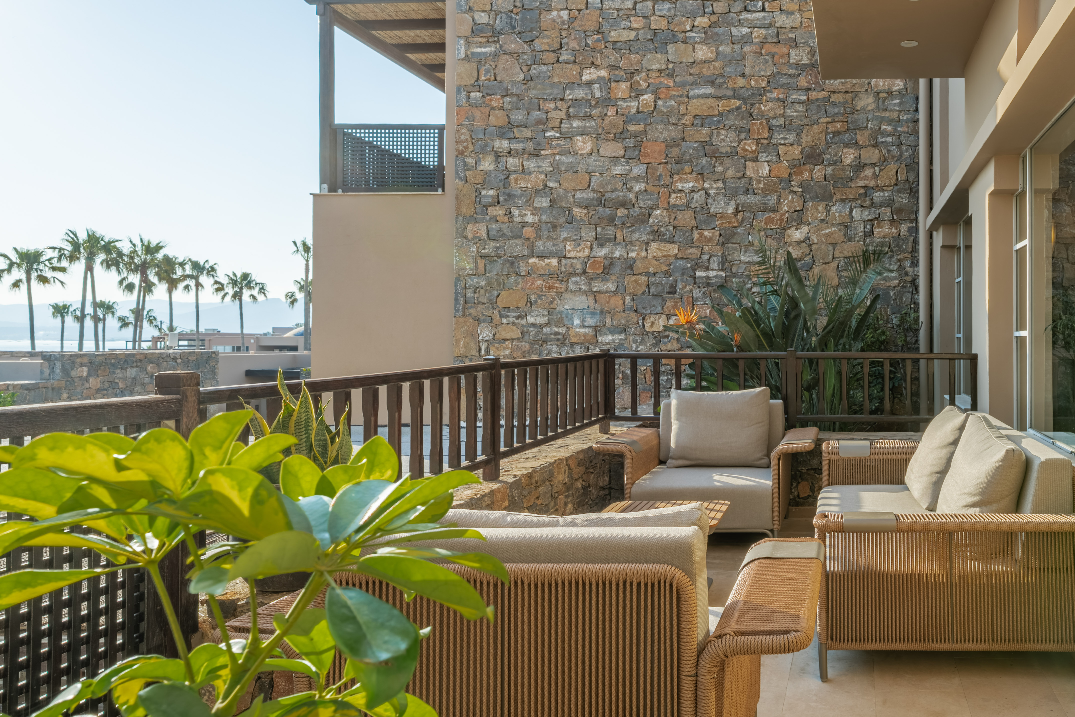 Resort balcony with elegant outdoor seating, stone wall, and tropical sea view.