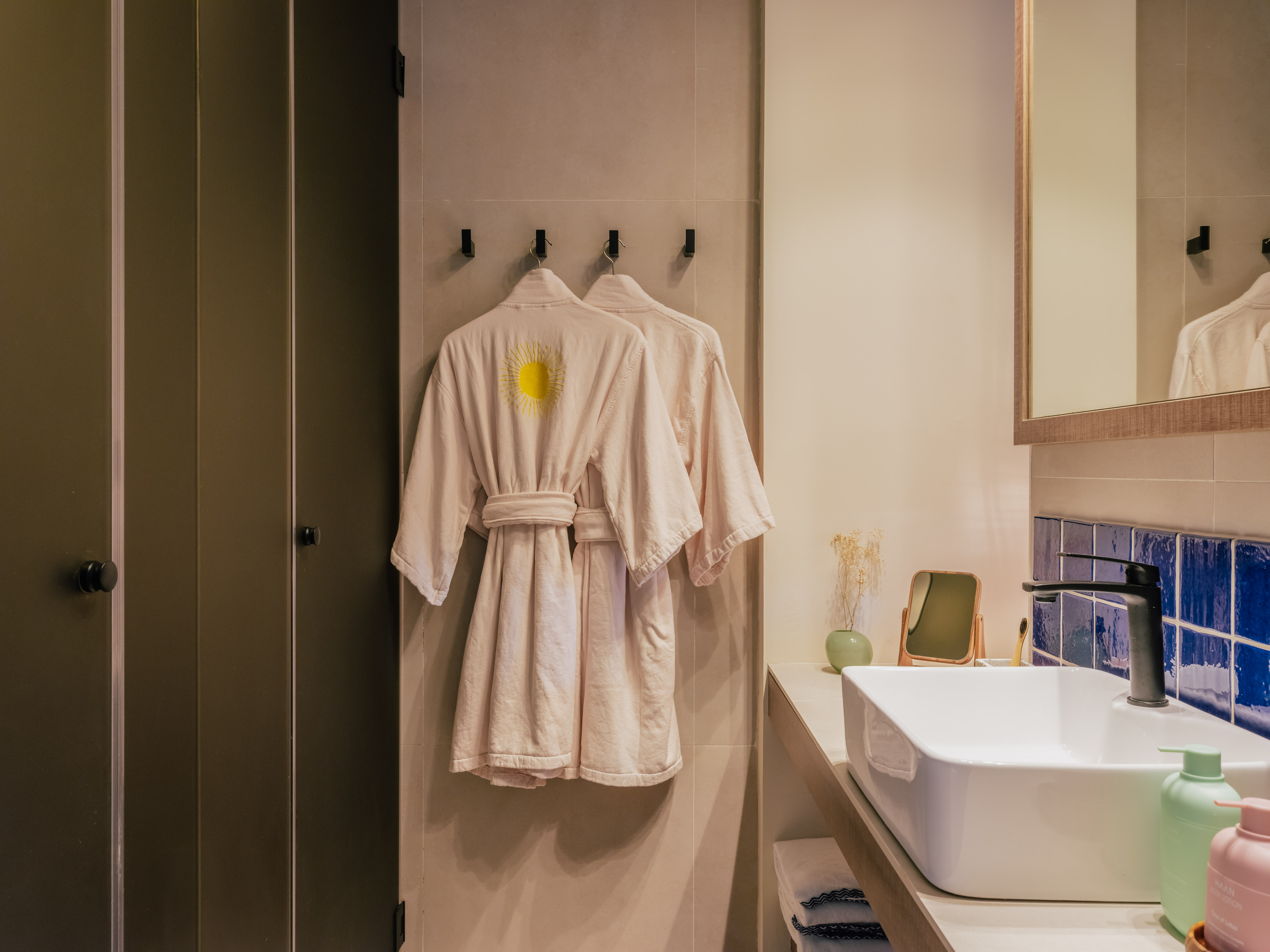 Modern bathroom: two bathrobes, white sink, blue tile backsplash, shower.