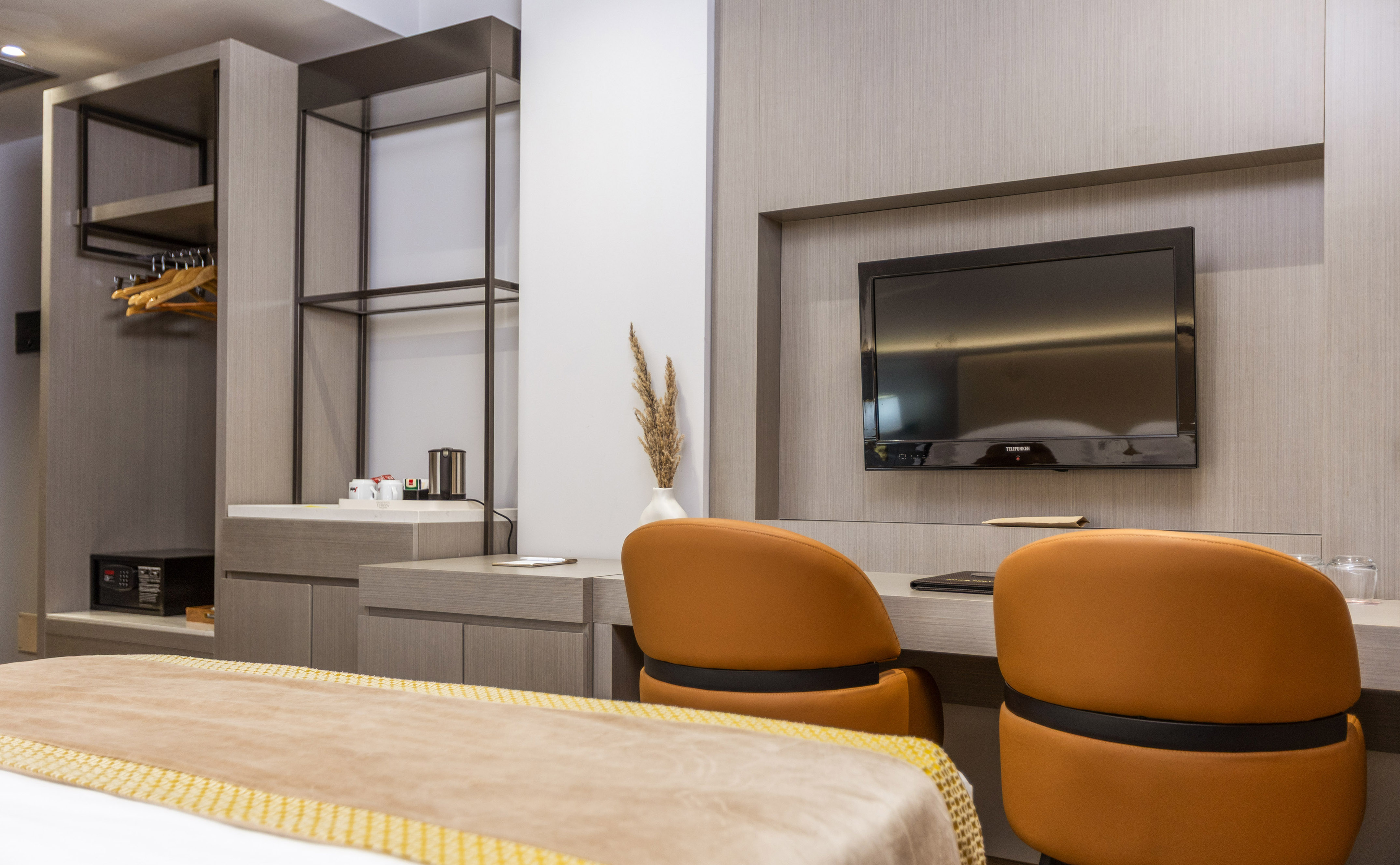 Modern hotel room with integrated desk, chairs, wall TV, and open closet.