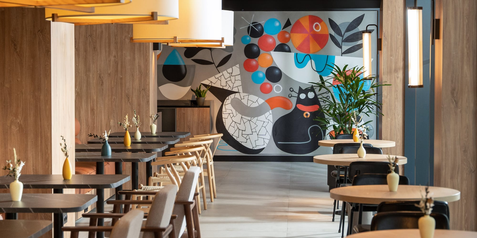Modern restaurant interior with wood walls and vibrant abstract cat mural.