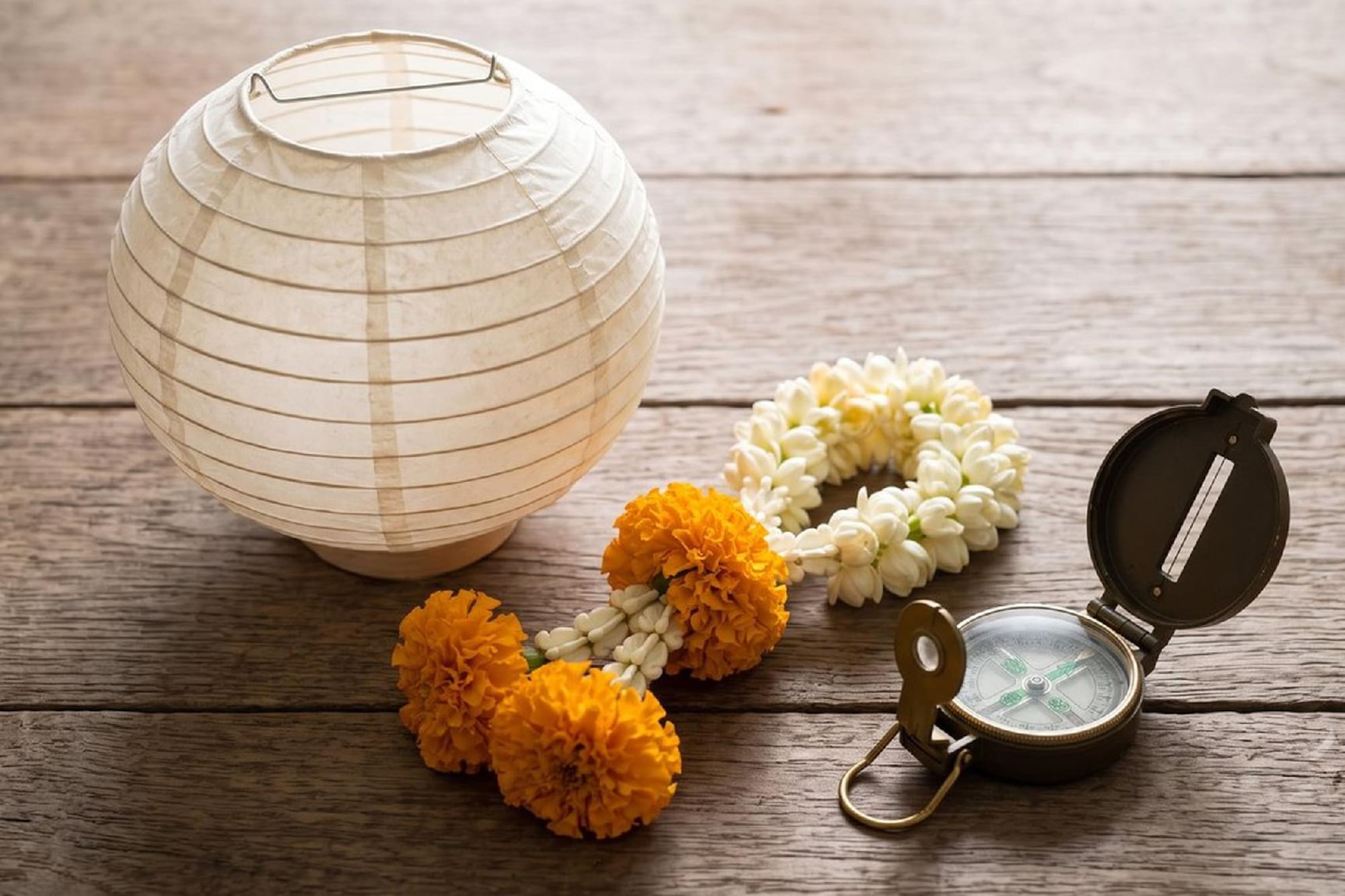 Lantern, jasmine & marigold garlands, and vintage compass on wooden table.