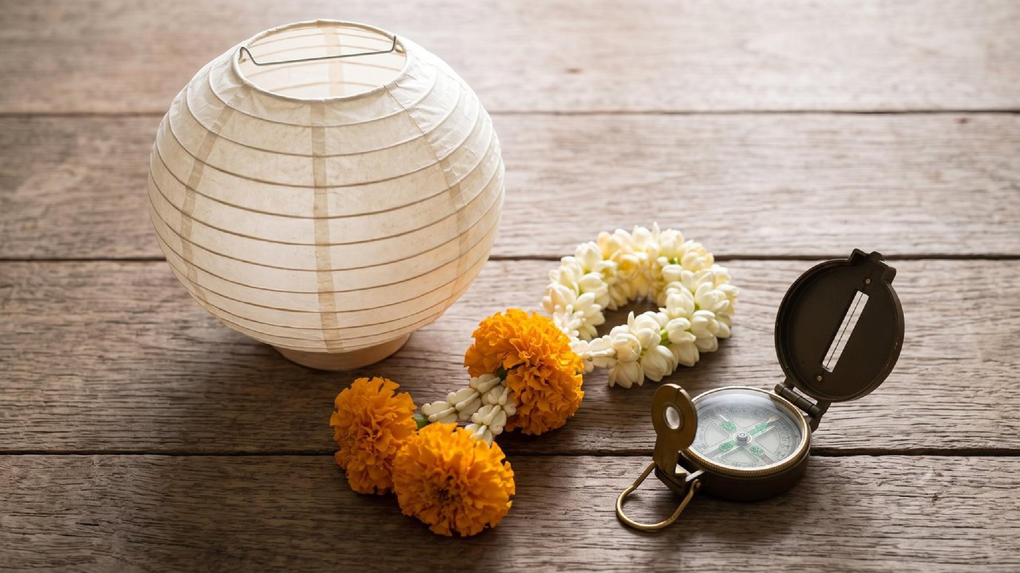 Lantern, jasmine & marigold garlands, and vintage compass on wooden table.