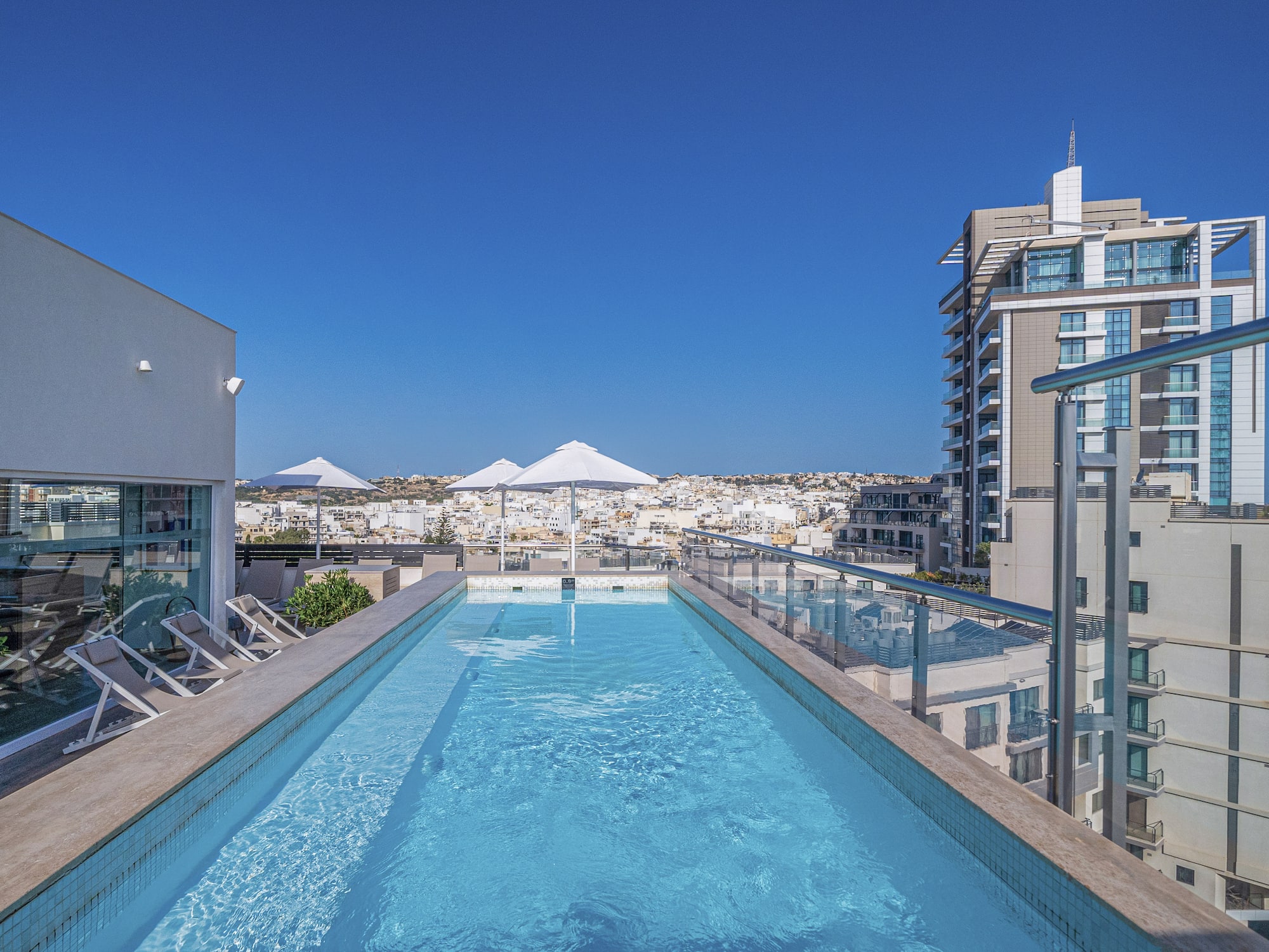 Sunny rooftop pool offering panoramic city views with modern buildings.