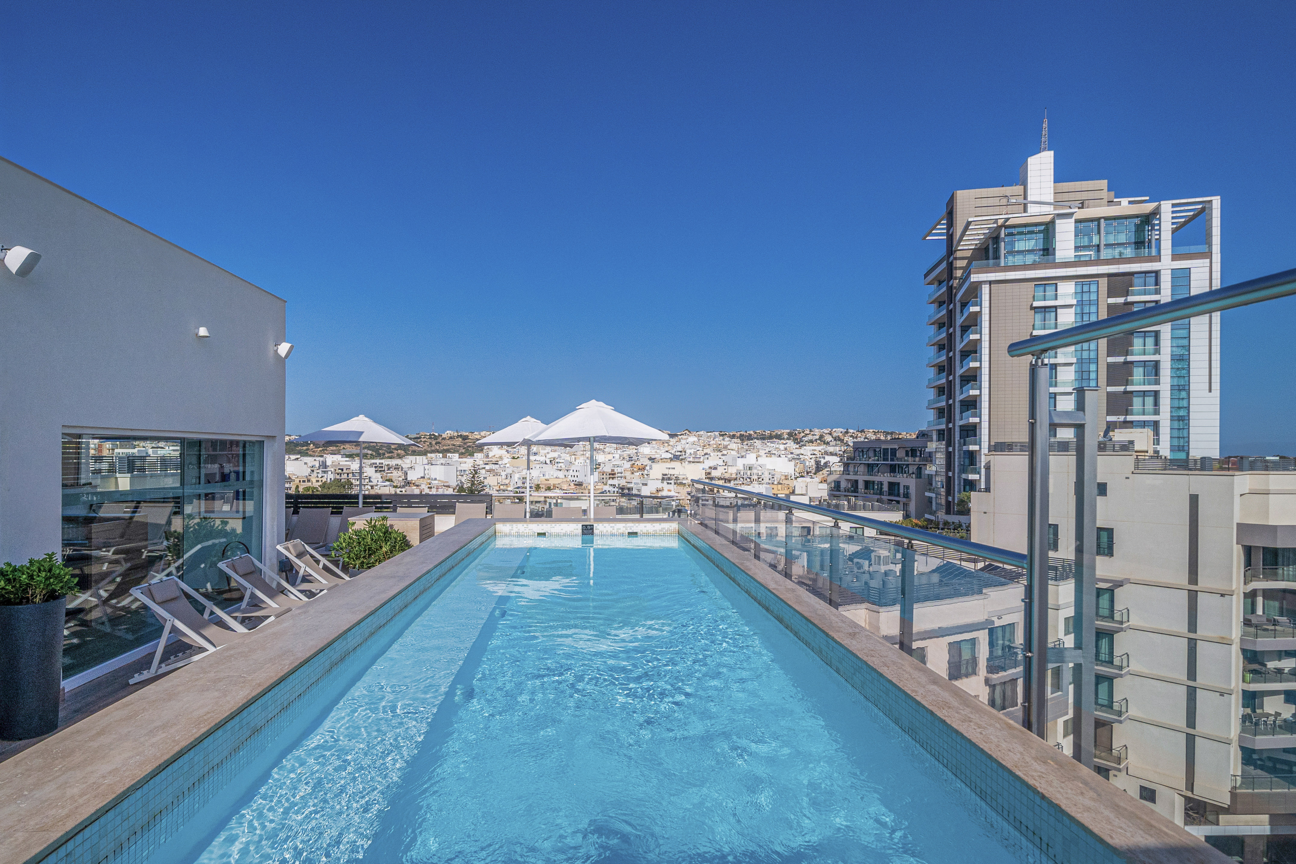 Sunny rooftop pool offering panoramic city views with modern buildings.