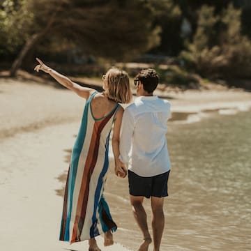 a man and woman holding hands and walking on a beach