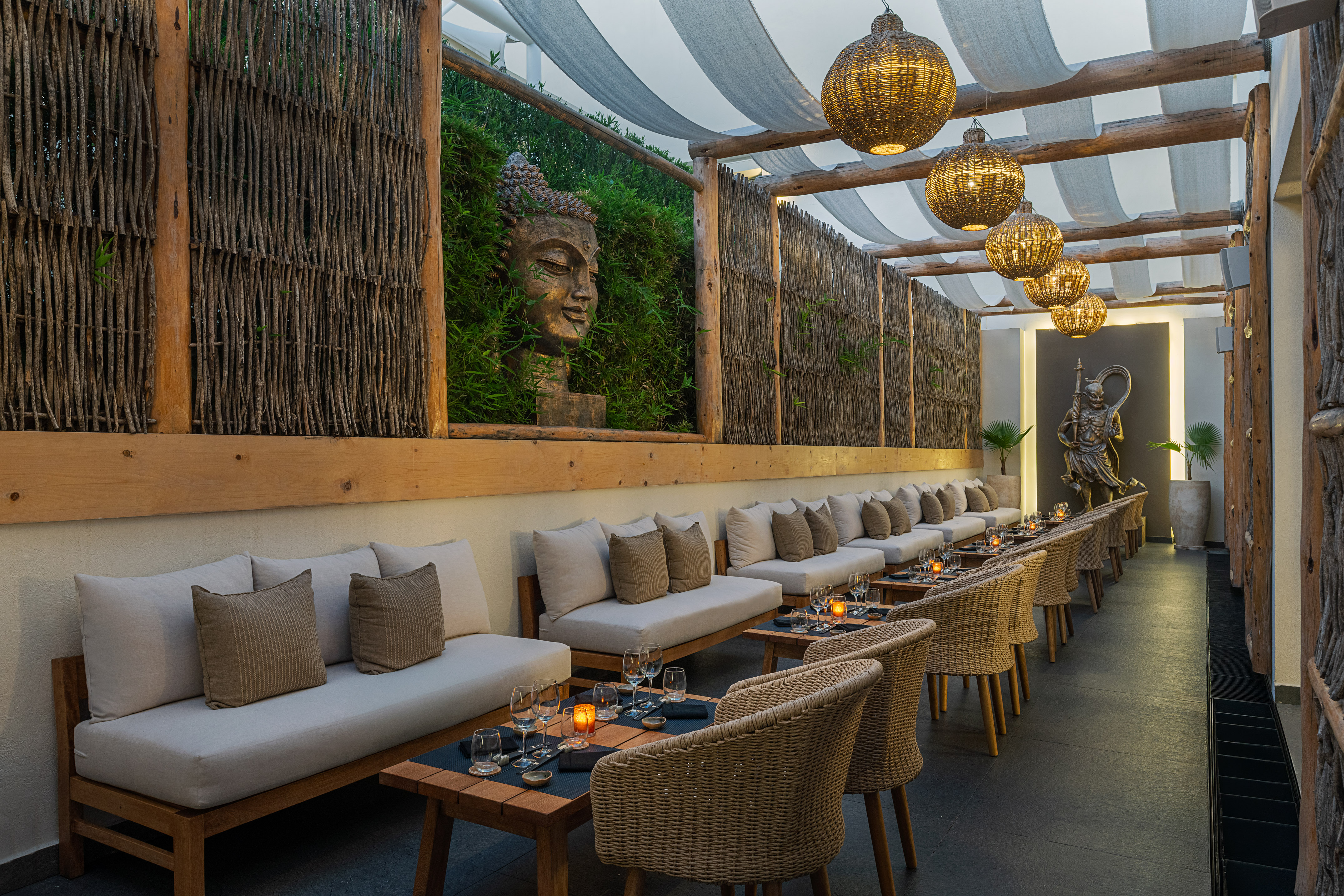 Outdoor restaurant lounge with Buddha statue, rattan lamps, and comfortable seating.