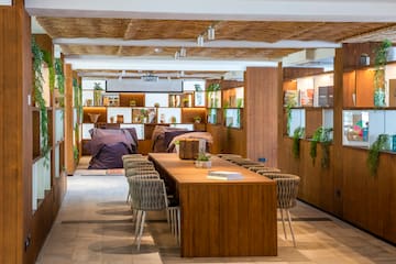 Modern lounge with wooden table, beanbags, green plants, and woven ceiling.